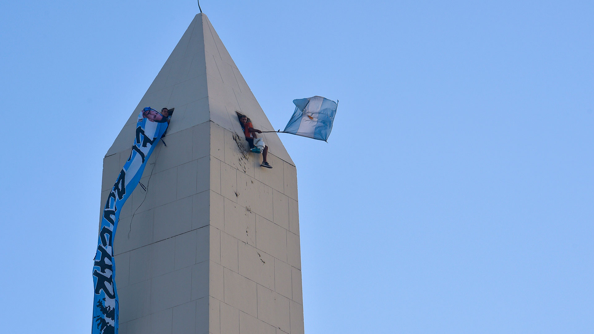 Hinchas que entraron en el Obelisco luego de romper la puerta de ingreso, muestran banderas desde las ventanas desafiando el peligro