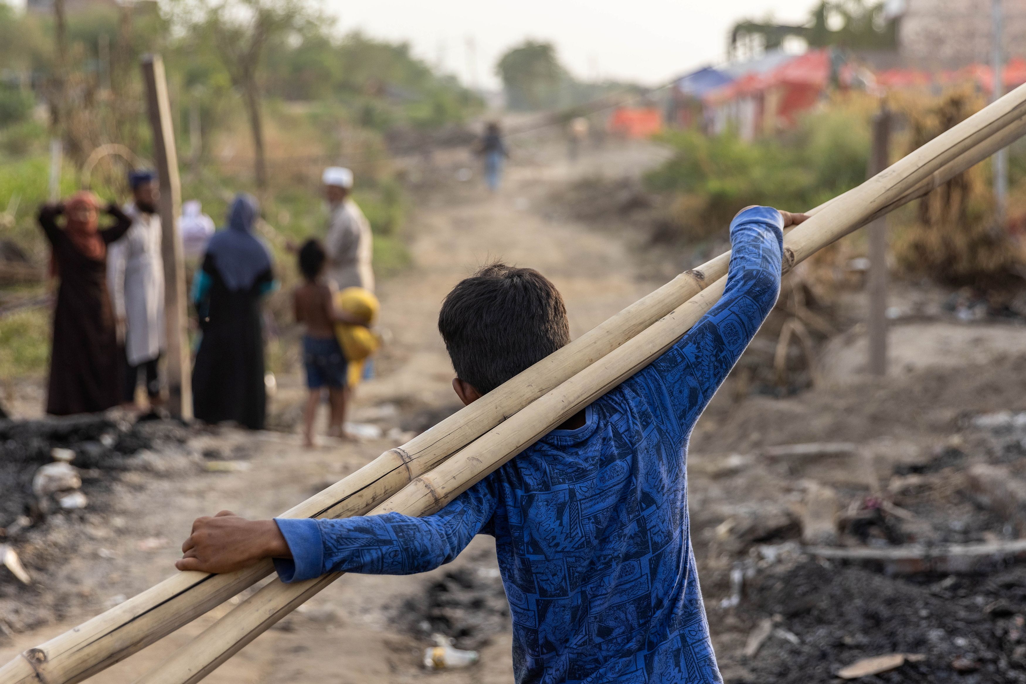 Un refugiado rohingya lleva palos de bambú a un refugio temporal después de que un incendio destruyera un campo de refugiados rohingya el sábado por la noche, en Nueva Delhi, India, 14 de junio de 2021.