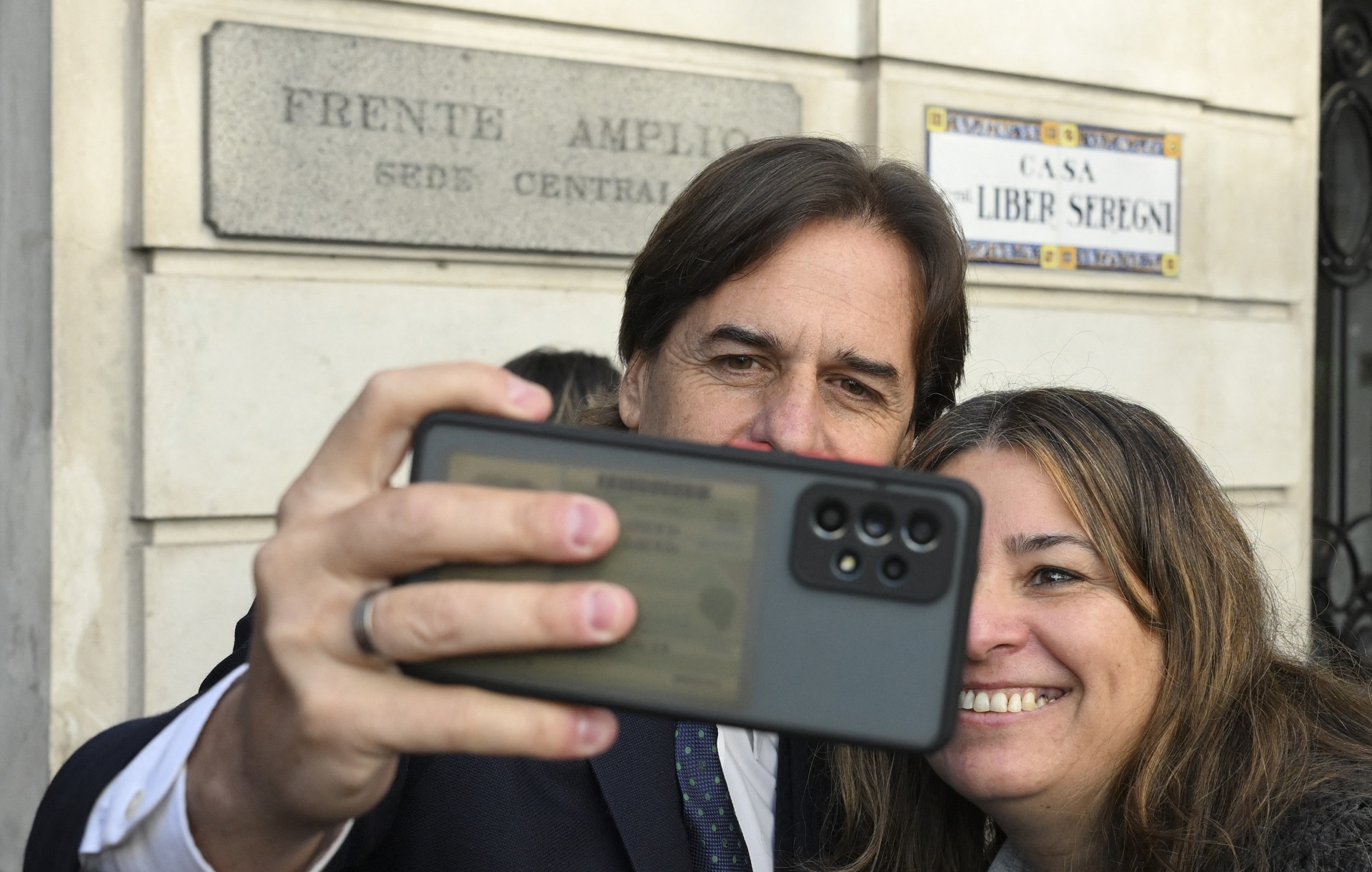 El momento capturado por la agencia AFP muestra al mandatario sacando él mismo la selfie con el teléfono de una mujer, militante opositora. De fondo, las placas dicen: “Frente Amplio, sede central” y “Casa Liber Seregni”.