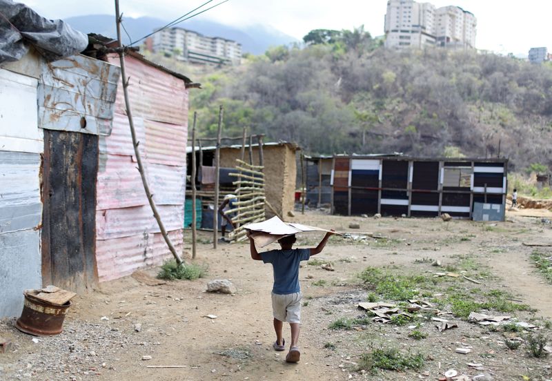 Foto de archivo ilustrativa de un niño llevando una lámina de hojalata cerca de un grupo de casas hechas con barro, palos y hojalata levantadas en un terreno baldío en el que las familias se establecen porque no pueden pagar un alquiler, en el municipio de Sucre, cerca de Caracas. 
Jun 12, 2020. REUTERS/Manaure Quintero