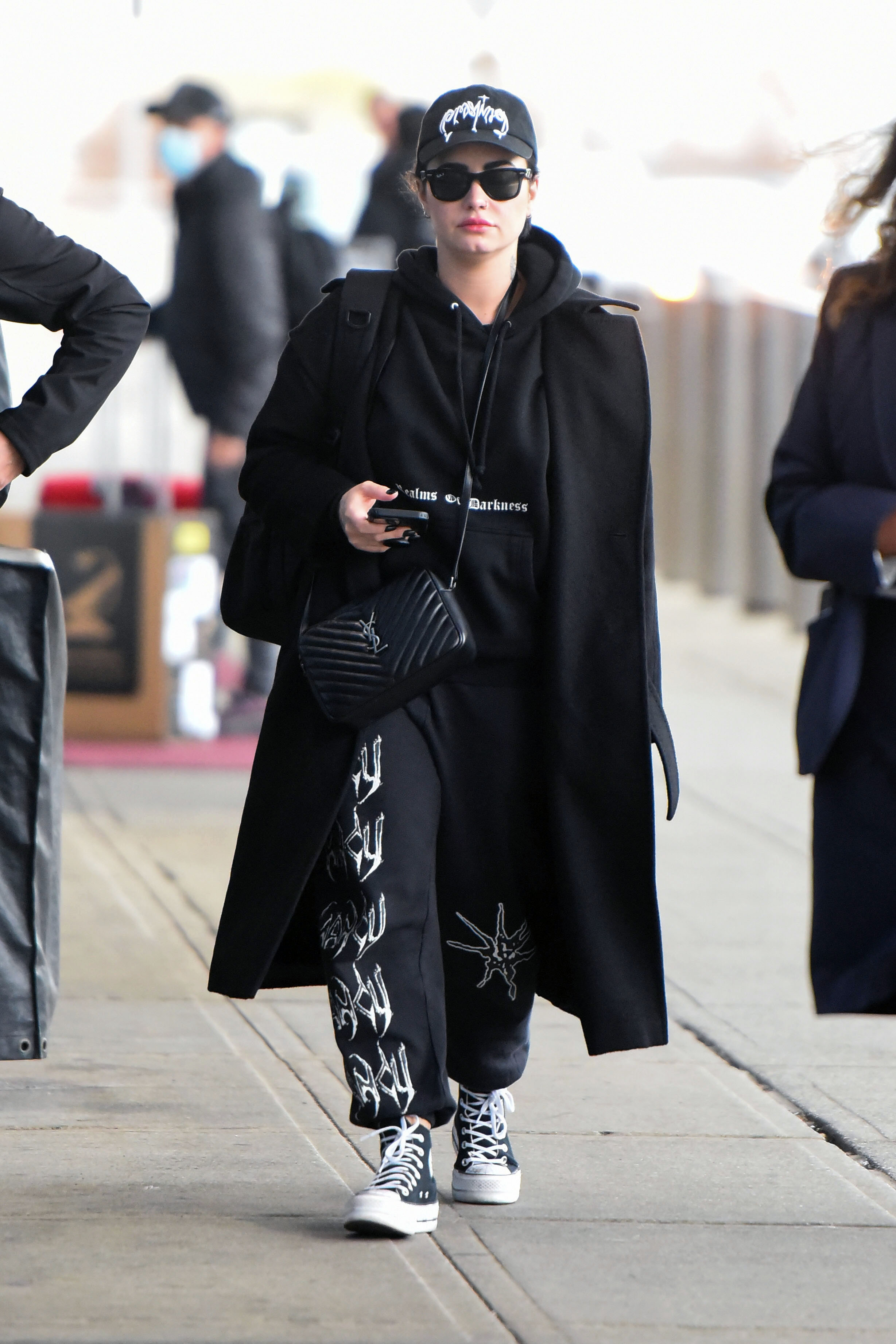 La cantante Demi Lovato, de 30 años, fue vista en las inmediaciones del aeropuerto JFK con una gorra negra combinada con un buzo y pantalones de chándal negros de Realms of Darkness, Chuck Taylors negras y un bolso de Yves St Laurent