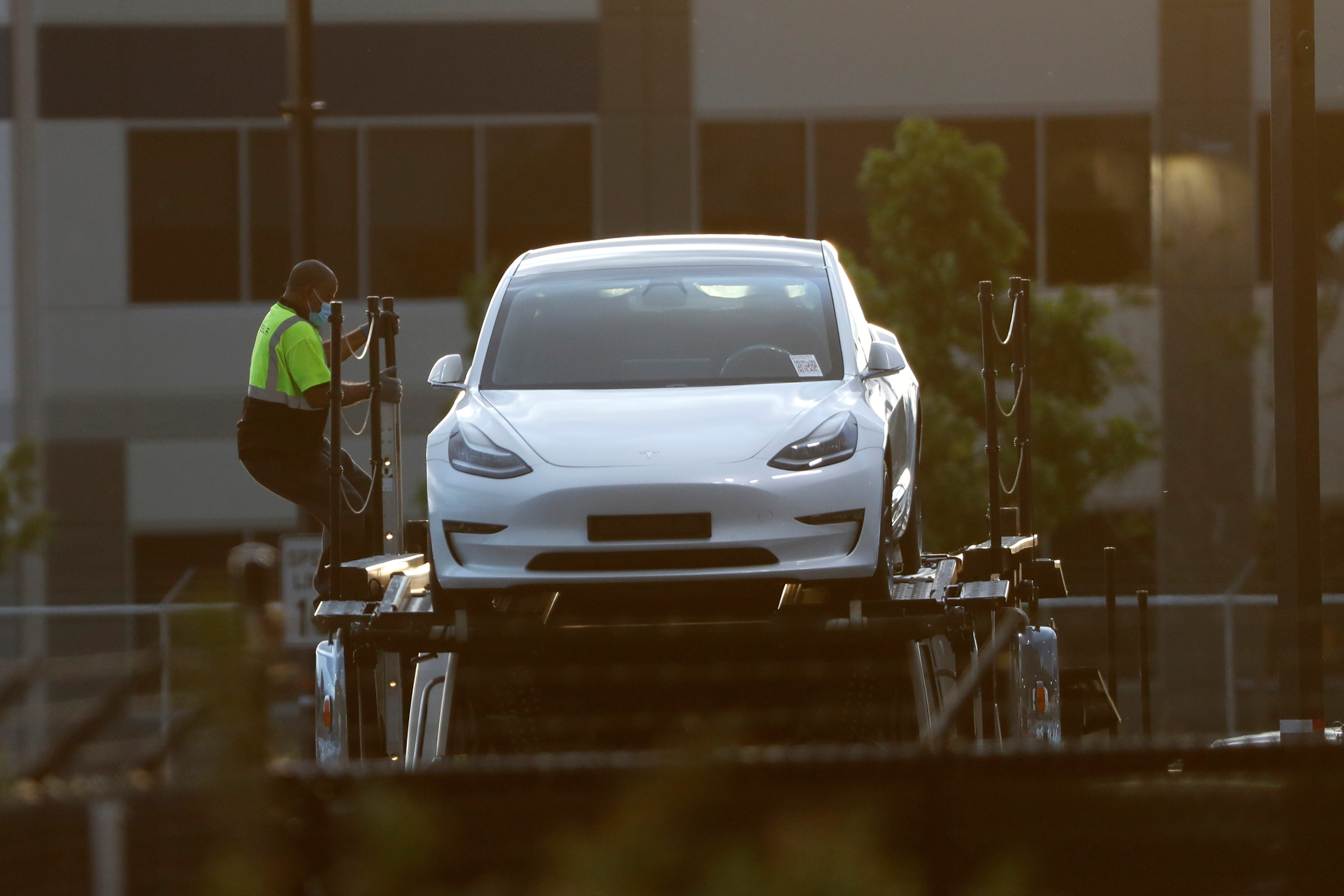 Un operario desciende de un trailer de carga de autos, tras subir un Model 3 de Tesla. (Reuters) 