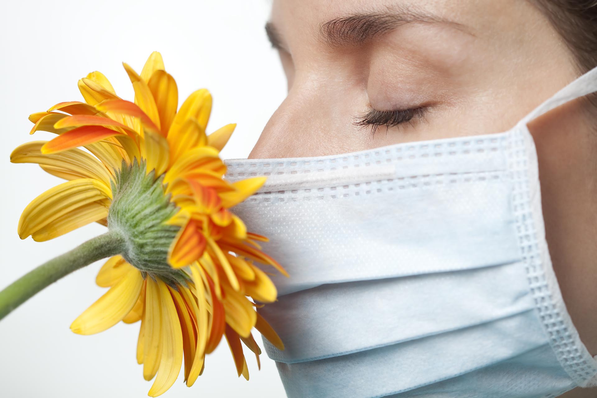 Woman smelling a flower while wearing a surgical mask.  You may also like: