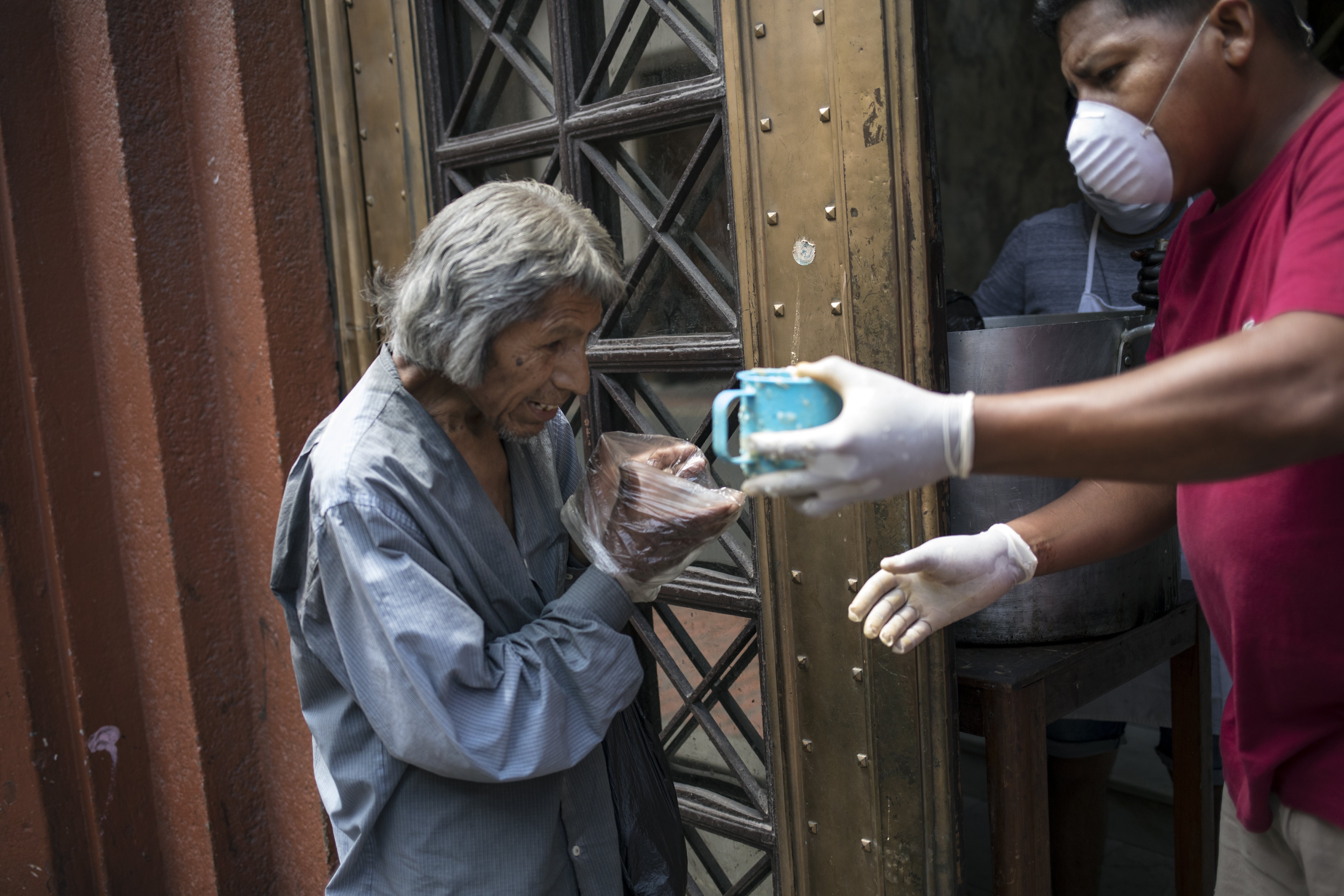 Un hombre utiliza bolsas de plástico como guantes desechables improvisados para tomar una taza de sopa gratis, en Lima, Perú, el jueves 26 de marzo de 2020, durante el confinamiento para frenar los contagios del nuevo coronavirus. (AP Foto/Rodrigo Abd)