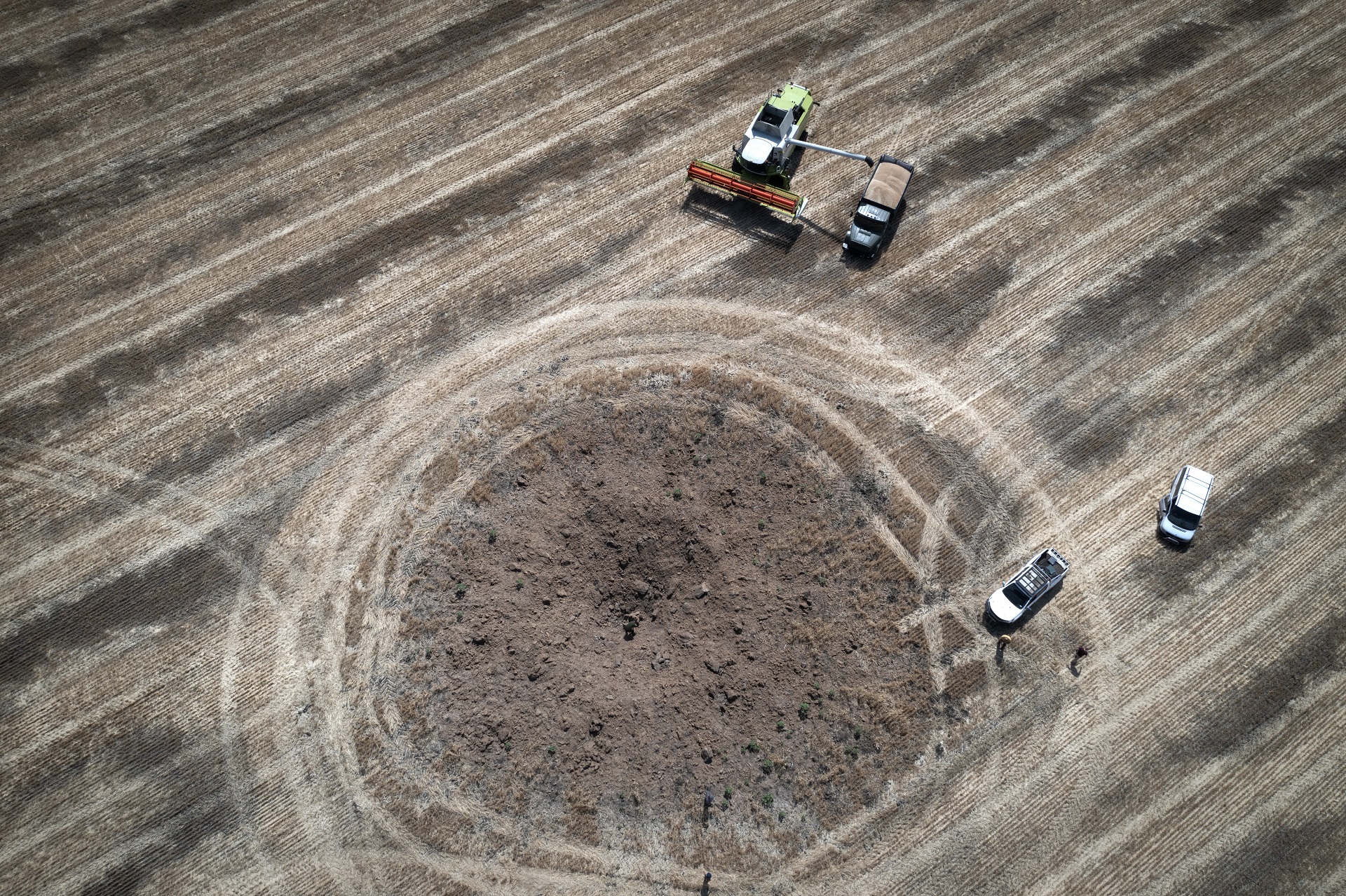 Un cráter provocado por un cohete ruso se ve mientras un agricultor cosecha un campo a 10 kilómetros del frente, donde hay fuertes combates, en la región de Dnipropetrovsk (AP Foto/Efrem Lukatsky)