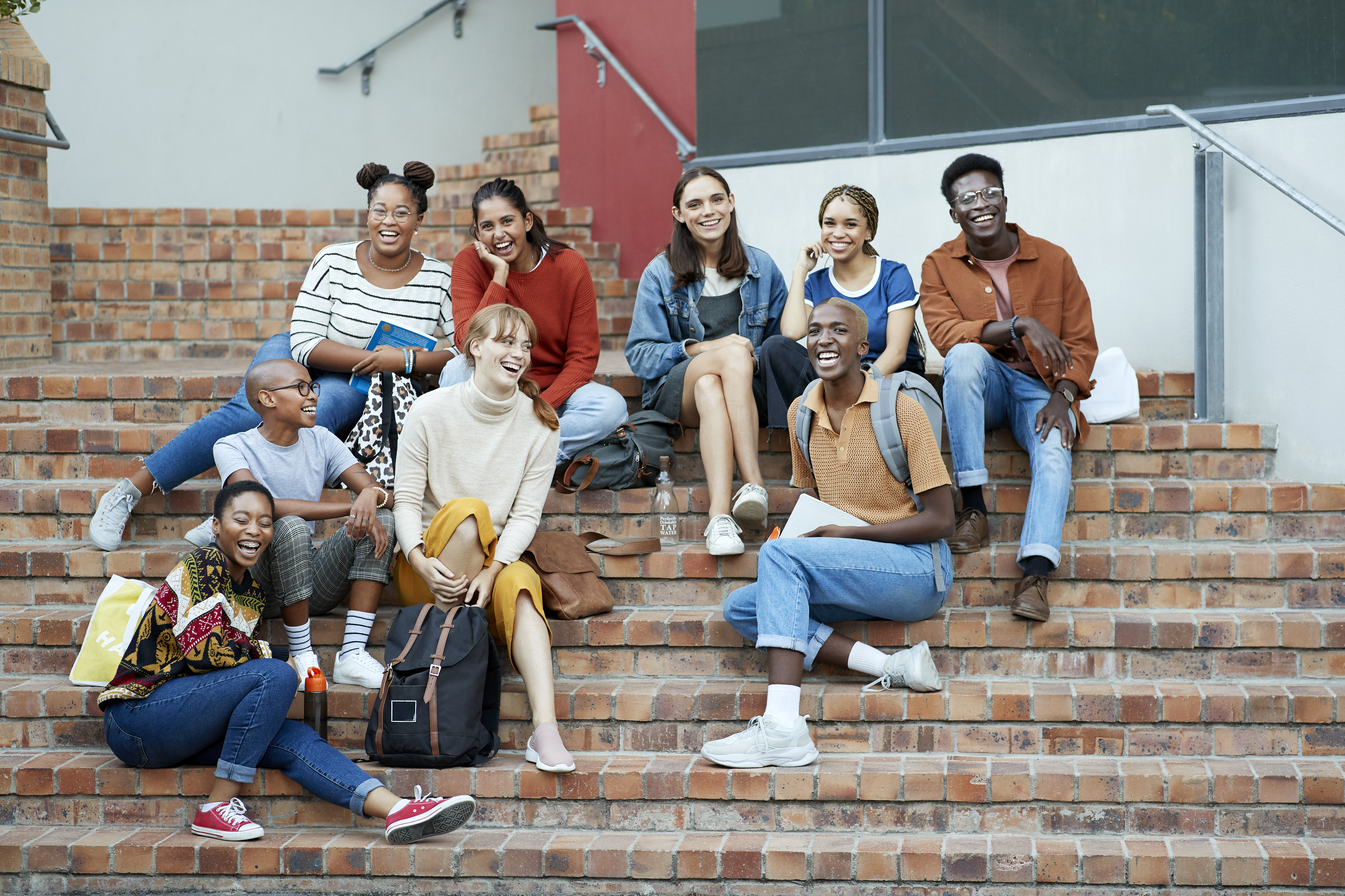 Full length of smiling young multi-ethnic male and female university students sitting on steps at community college