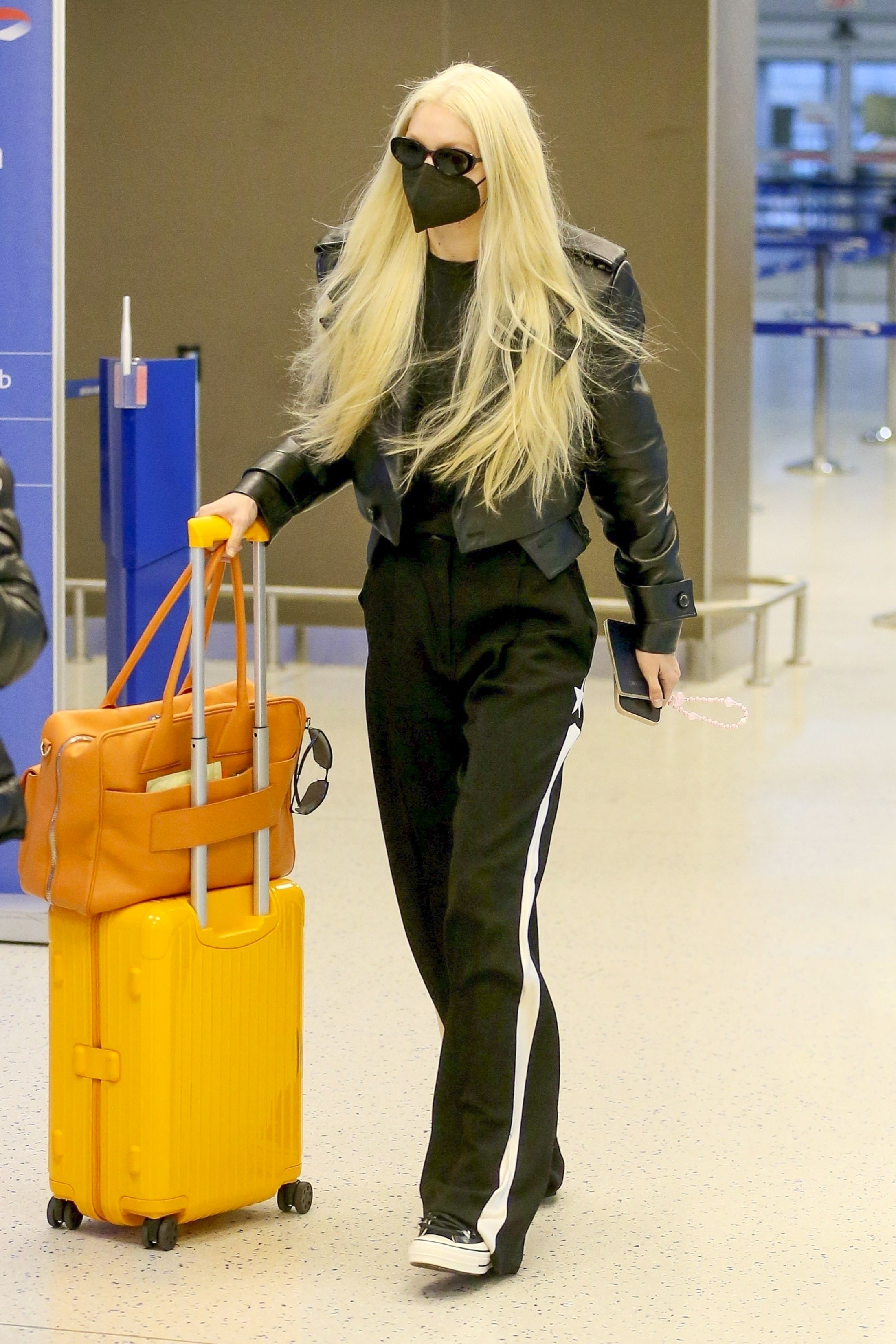 Gigi Hadid fue fotografiada en el aeropuerto de Nueva York. Para viajar, eligió un look cómodo: pantalón deportivo, remera negra y campera de cuero del mismo color. En tanto, su valija de mano era color amarillo y su cartera, naranja
