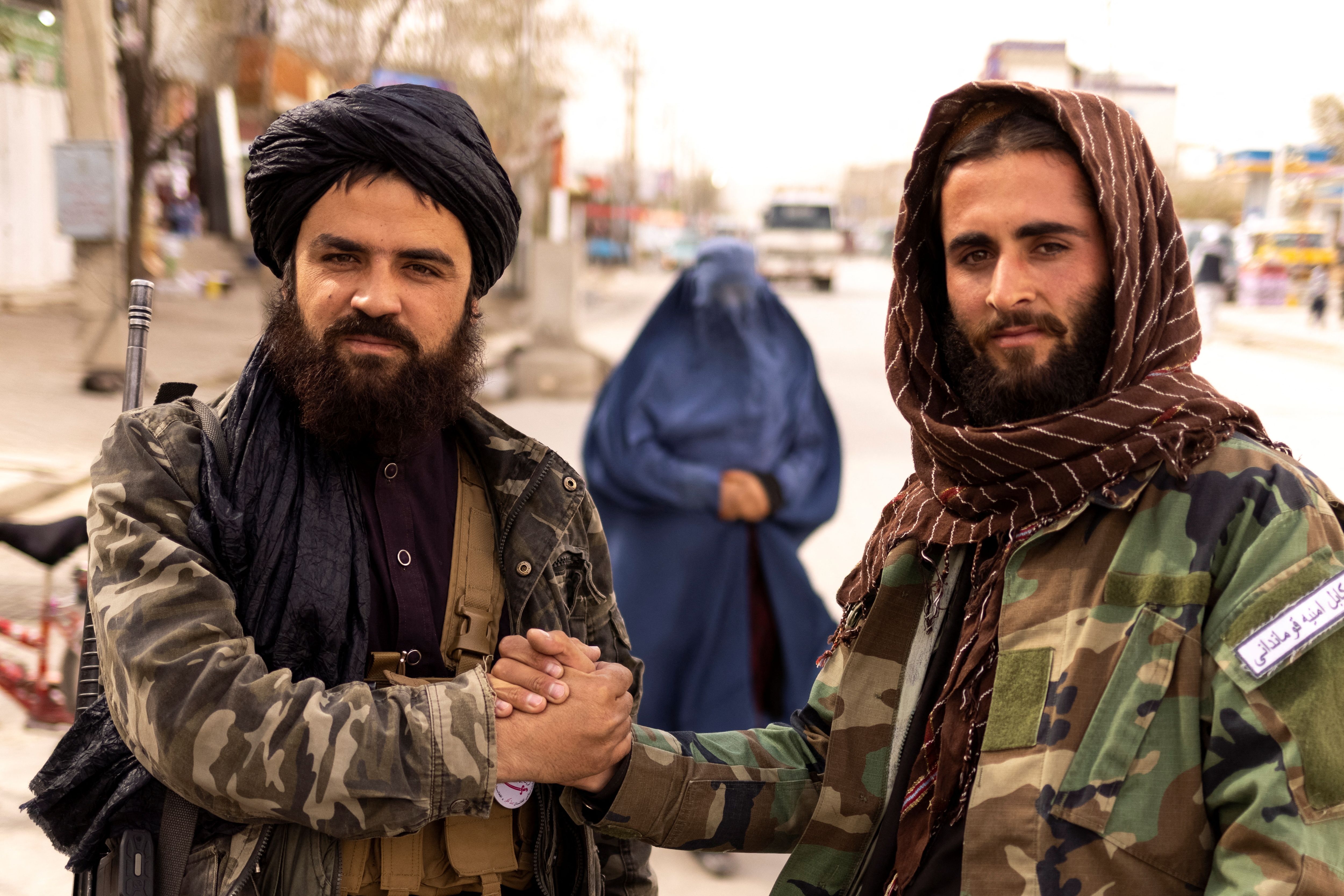 Los miembros talibanes Muhammad Aref y Junaid se saludan en un puesto de control, mientras una mujer con burka camina detrás de ellos, en Kabul, Afganistán, el 22 de octubre de 2021. Imagen tomada el 22 de octubre de 2021. REUTERS/Jorge Silva