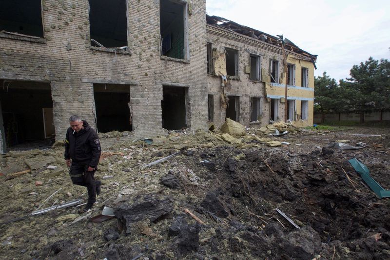 Un oficial de policía camina junto a un edificio escolar dañado por un ataque militar ruso