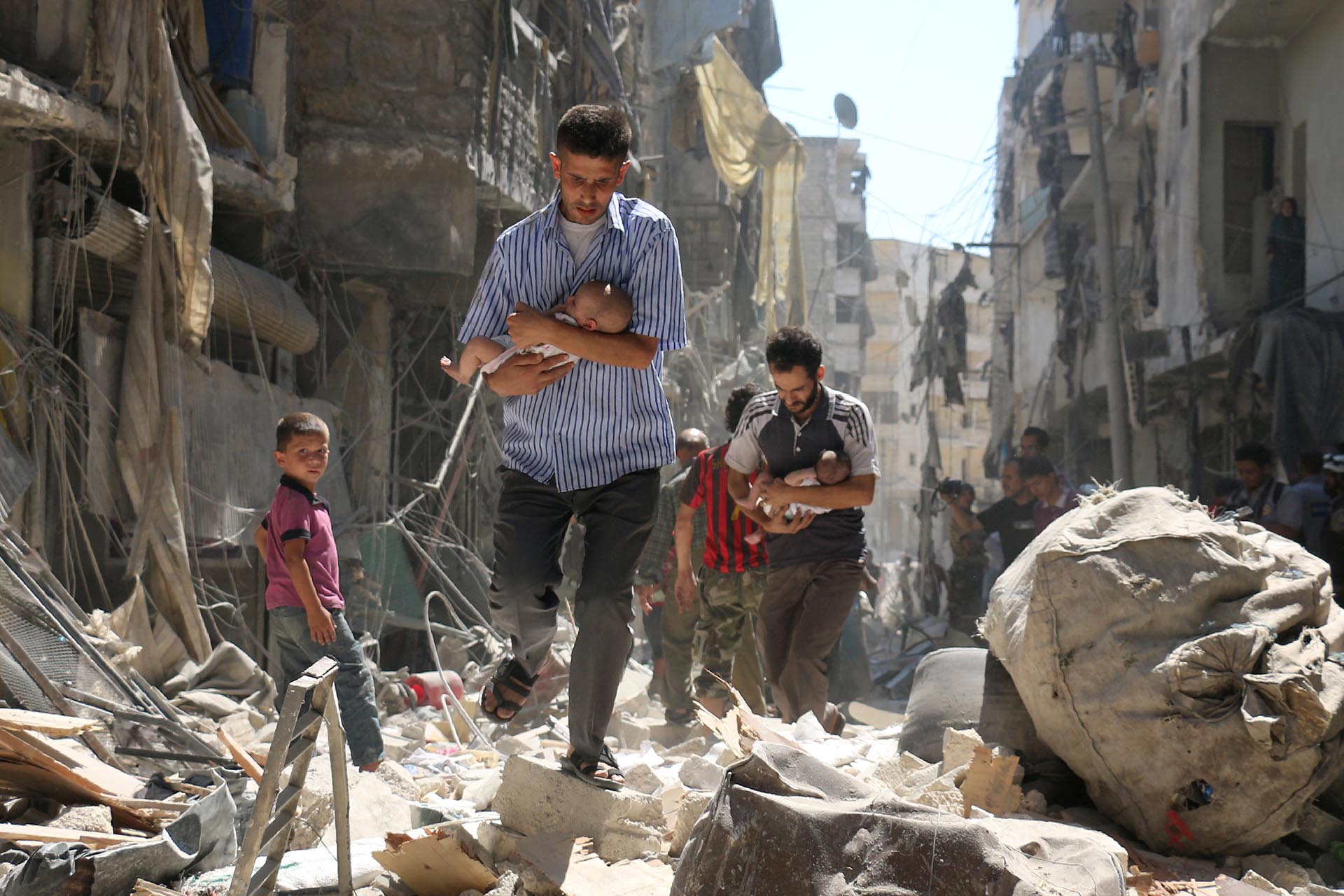 Hombres sirios con bebés se abren paso entre los escombros de edificios destruidos tras un ataque aéreo contra el barrio rebelde de Salihin, en Alepo, el 11 de septiembre de 2016 (REUTERS)