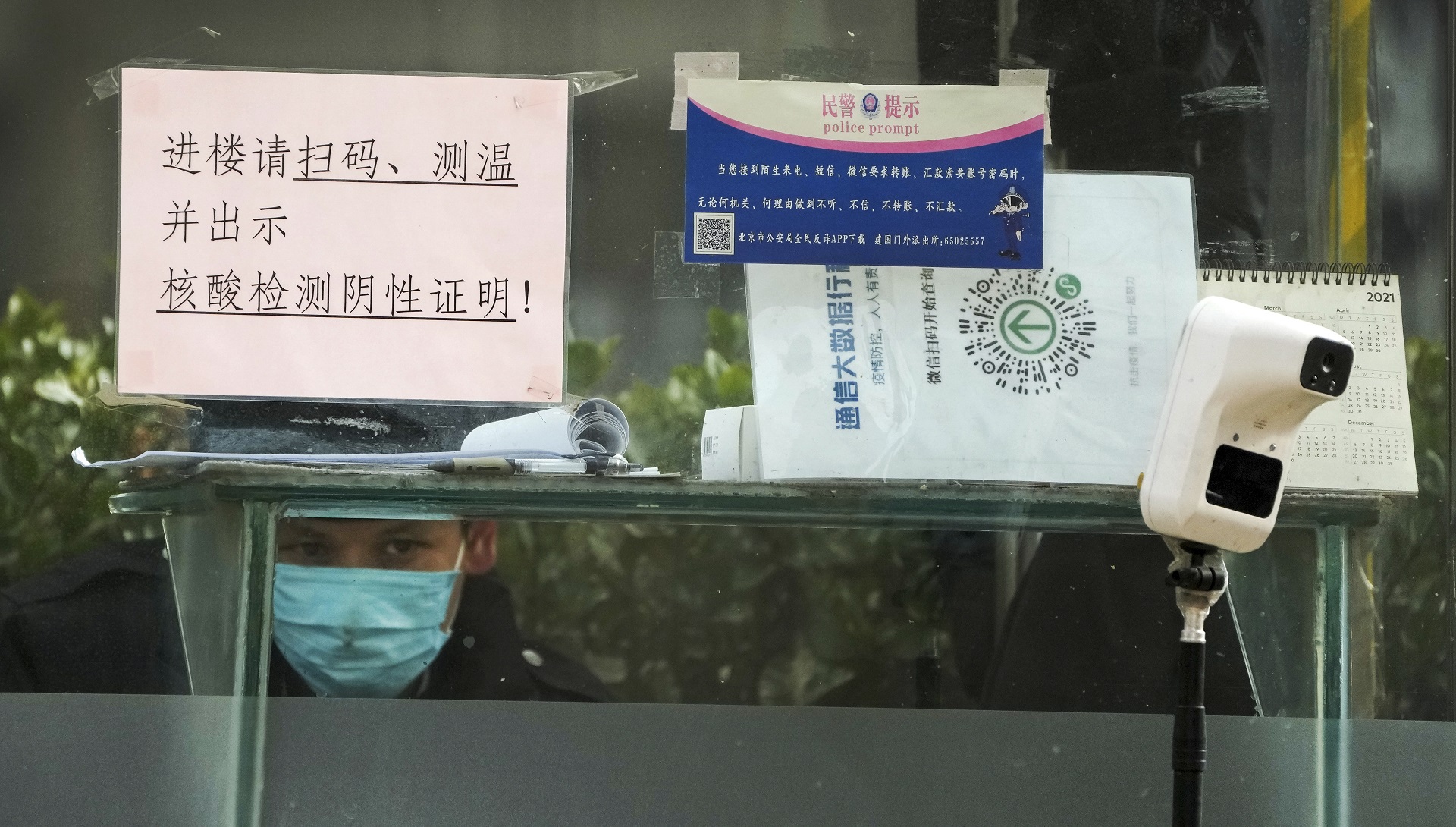 Un guardia de seguridad vigila desde dentro de una cabina con un dispositivo de control de temperatura y un lector QR para registrar desplazamientos, ante un edificio de oficinas de Beijing, el lunes 12 de diciembre de 2022. (AP Foto/Andy Wong)