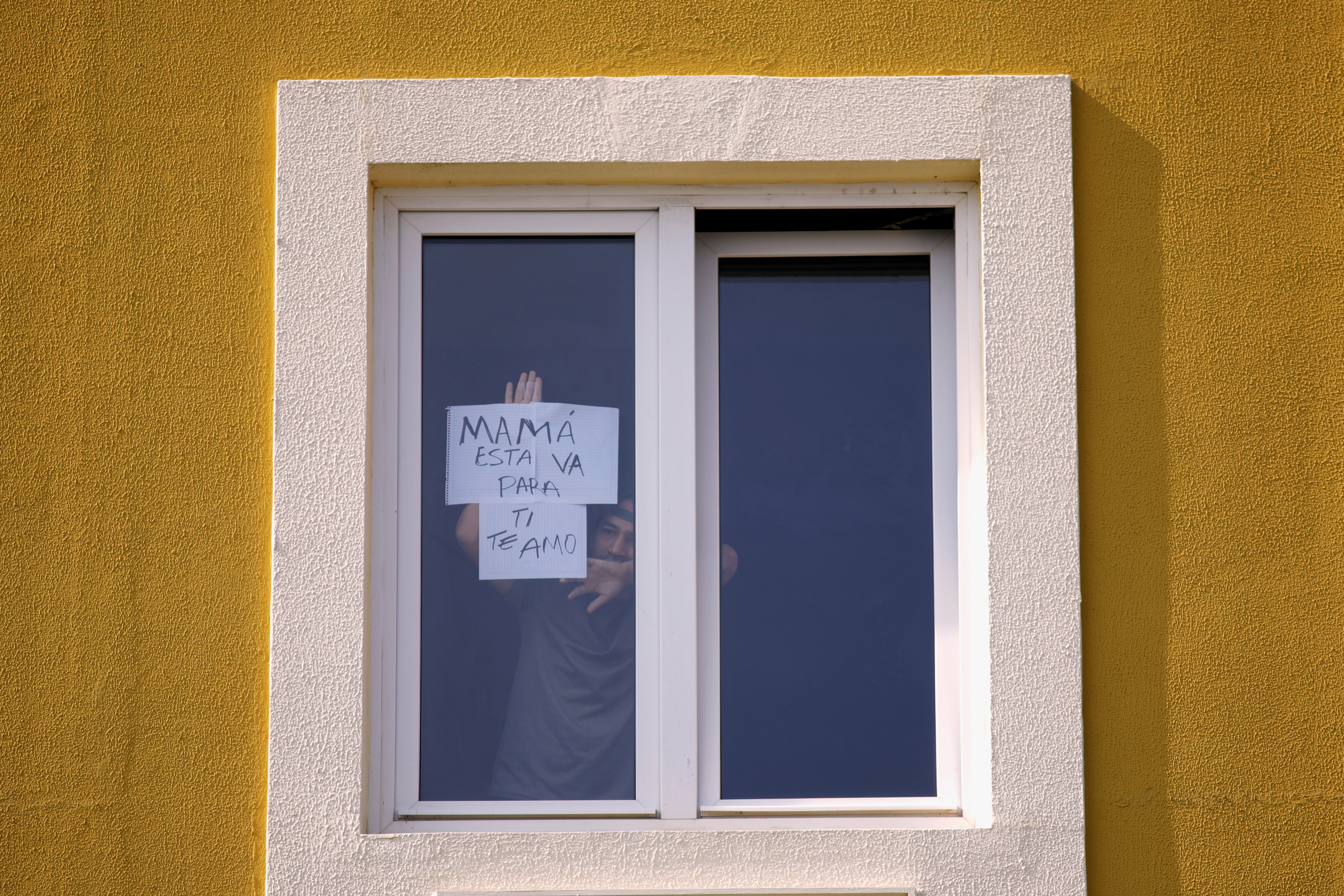 Un paciente aislado en un hotel, utilizado como centro de cuarentena, muestra un letrero que dice en español:
