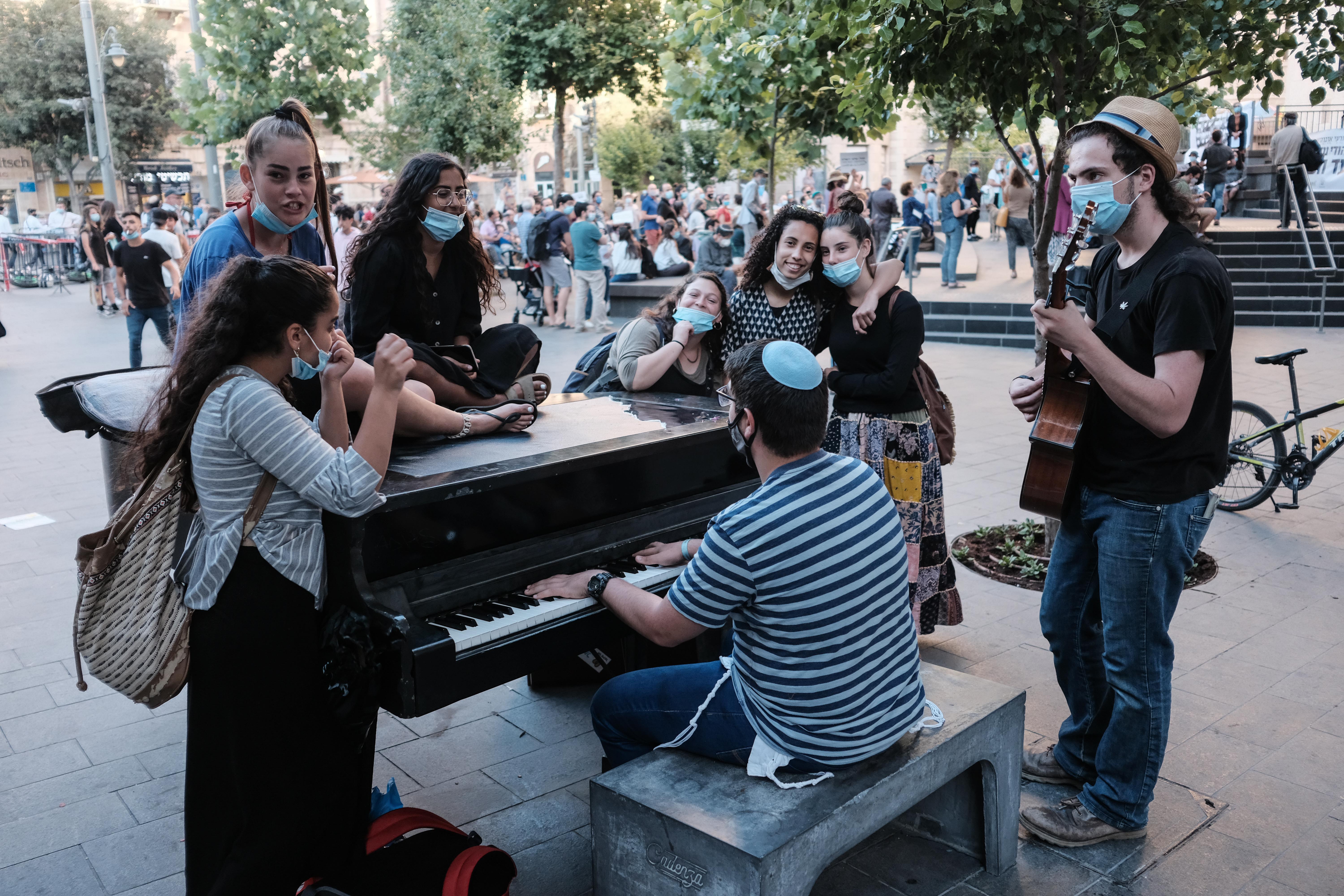 Un grupo de jóvenes usando máscaras se reúnen alrededor de un piano en Jerusalem, Israel. Photo: Nir Alon/ZUMA Wire/dpa