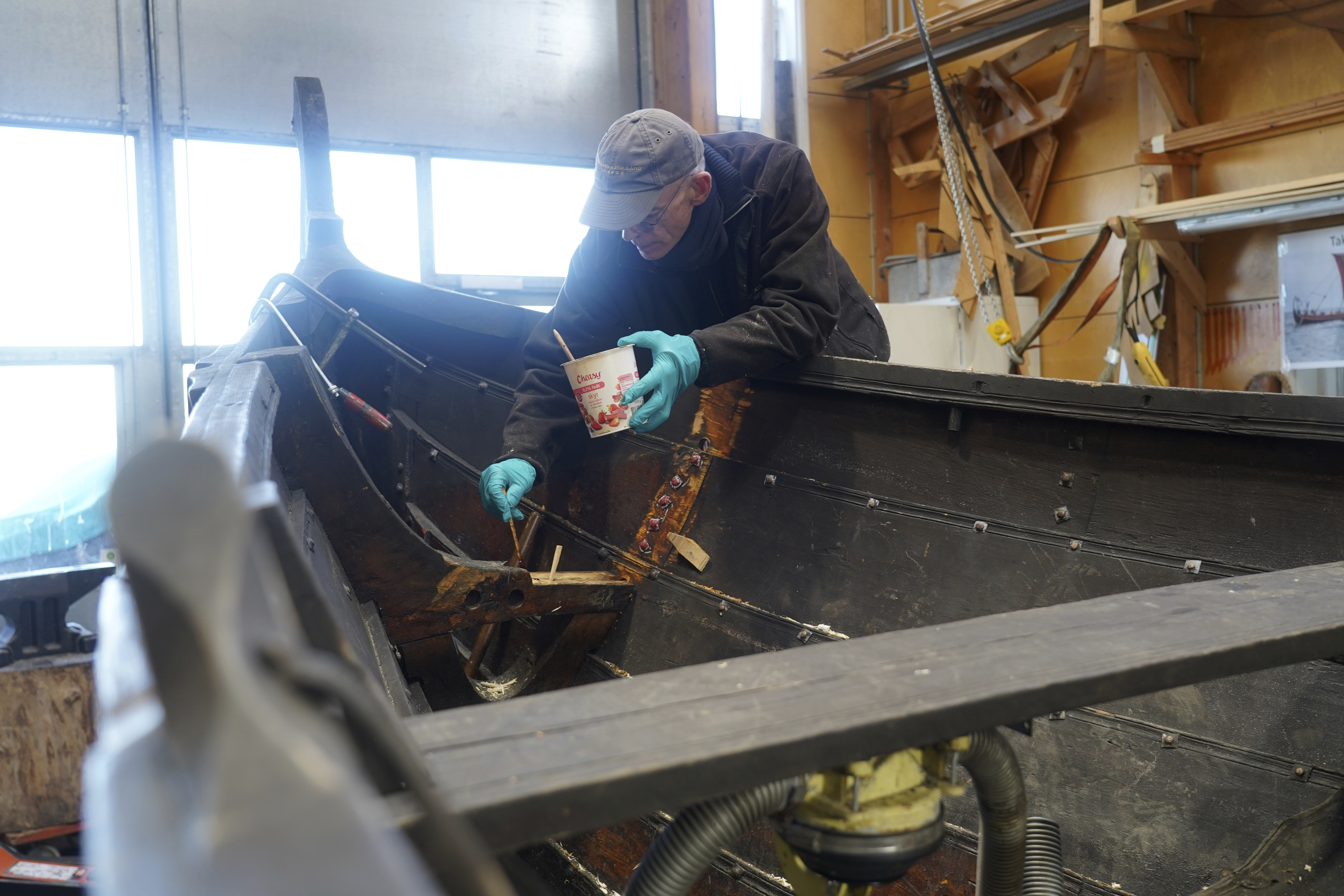 Un hombre repara un bote de remos de madera de 10 metros, construido según la tradición nórdica de los botes de escoria, en el astillero del Museo de Barcos Vikingos. Roskilde, Dinamarca, lunes 17 de enero de 2022. (Foto AP/James Brooks)