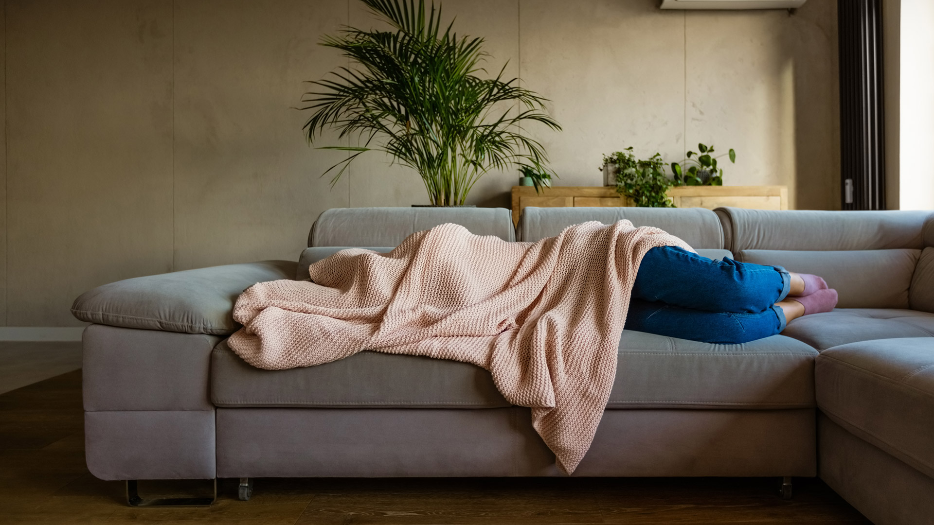 Young woman lying down on sofa in living room covered by blanket. Unrecognizable person.