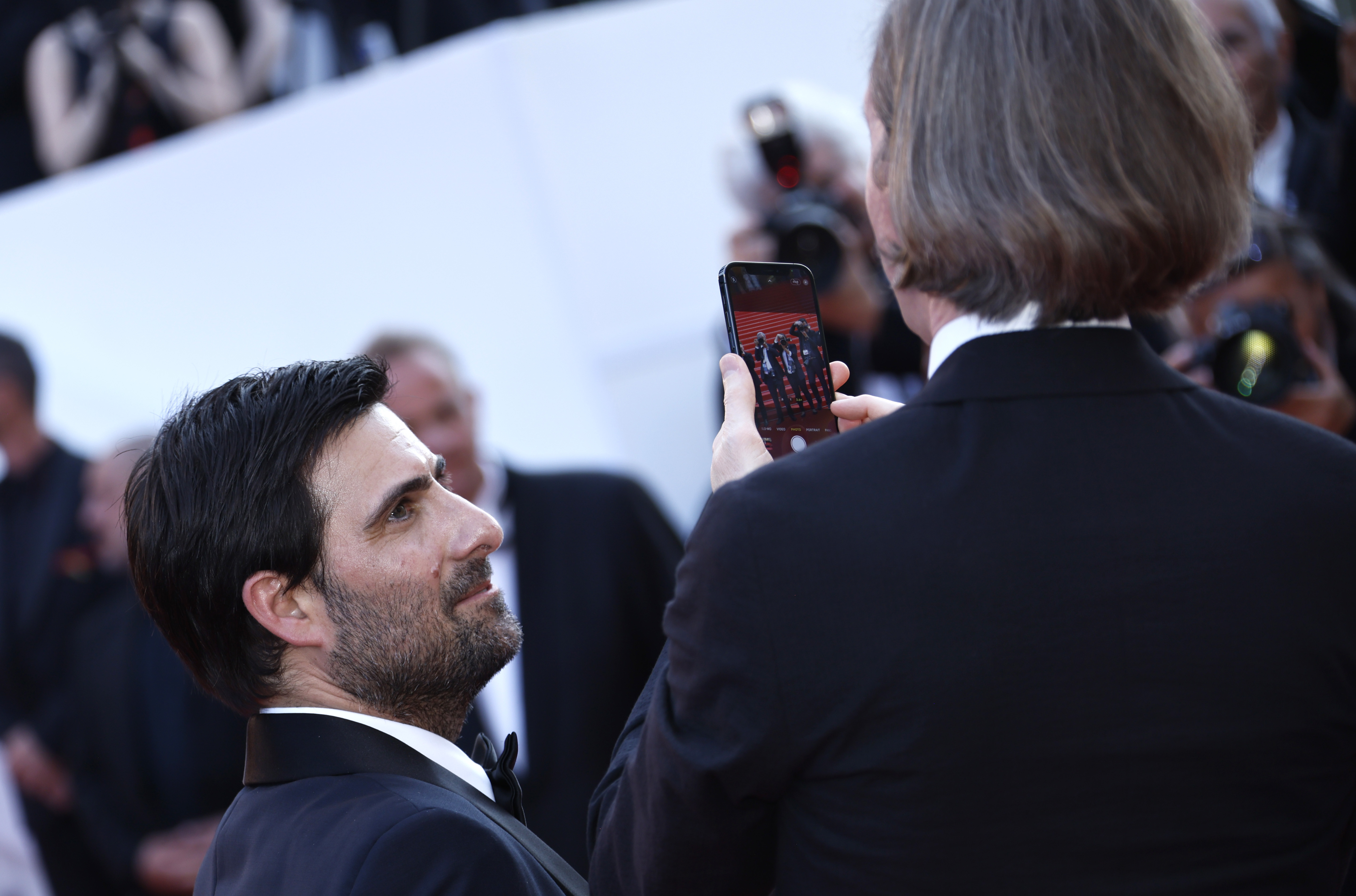 Wes Anderson, a la derecha, toma una fotografía a los fotógrafos de la alfombra roja mientras el actor Jason Schwartzman observa, al llegar al estreno de "Asteroid City" en Cannes 2023. (Foto: Joel C Ryan/Invision/AP)