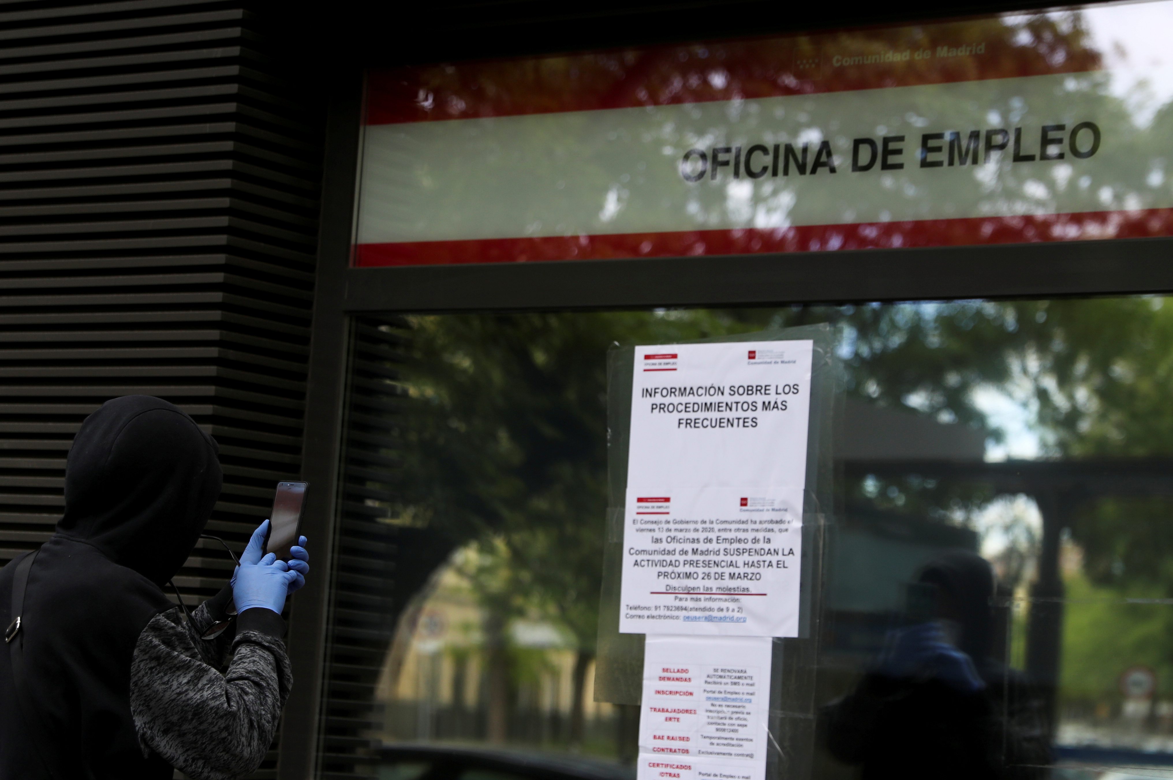 Un hombre con guantes protectores toma fotografías de un panel de información afuera de un centro para el empleo en Madrid, España, 28 de abril de 2020. (REUTERS / Susana Vera)