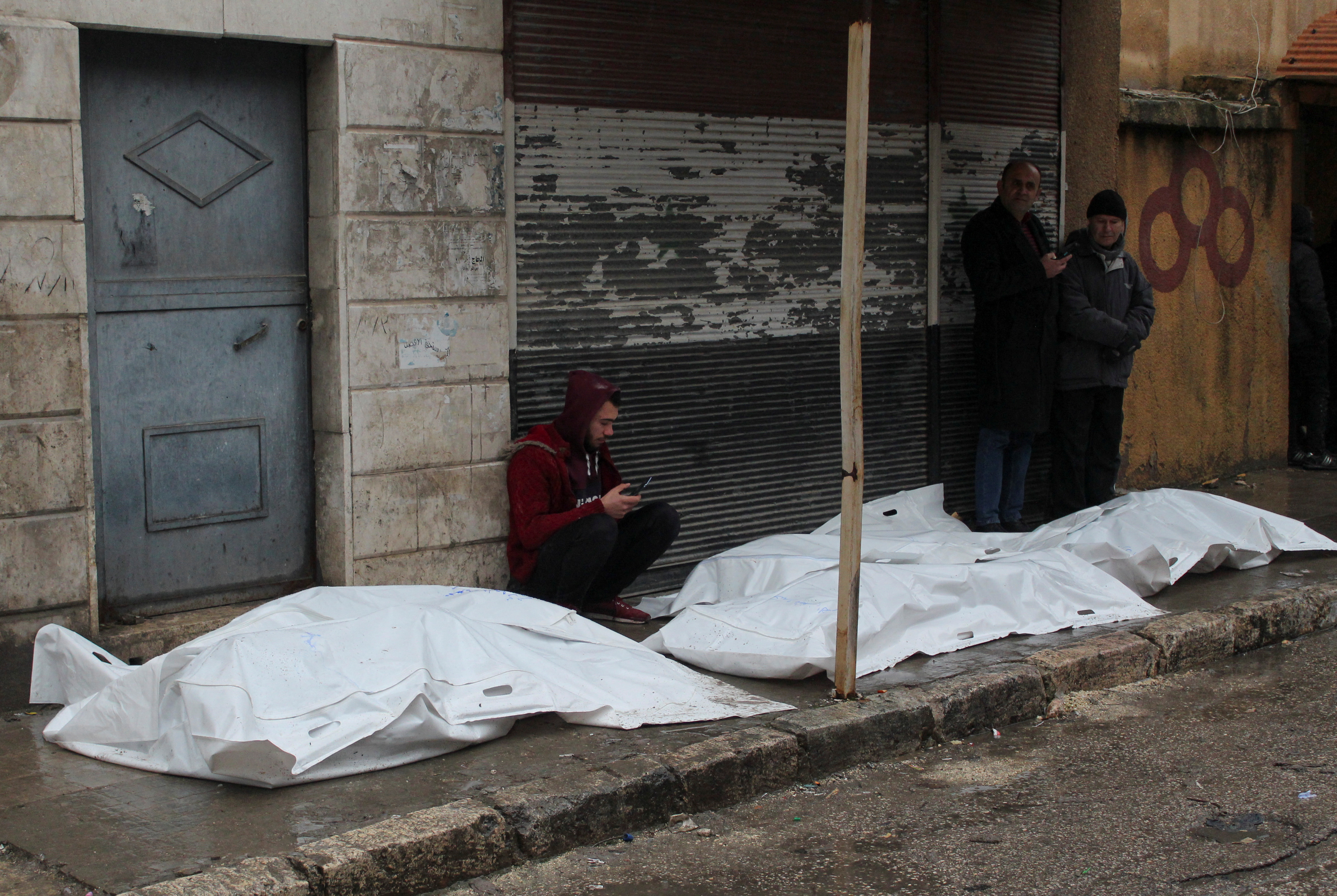 Un hombre se sienta junto a cadáveres en bolsas que yacen en el suelo, después de un terremoto, en Alepo, Siria, 6 de febrero de 2023. REUTERS/Firas Makdesi