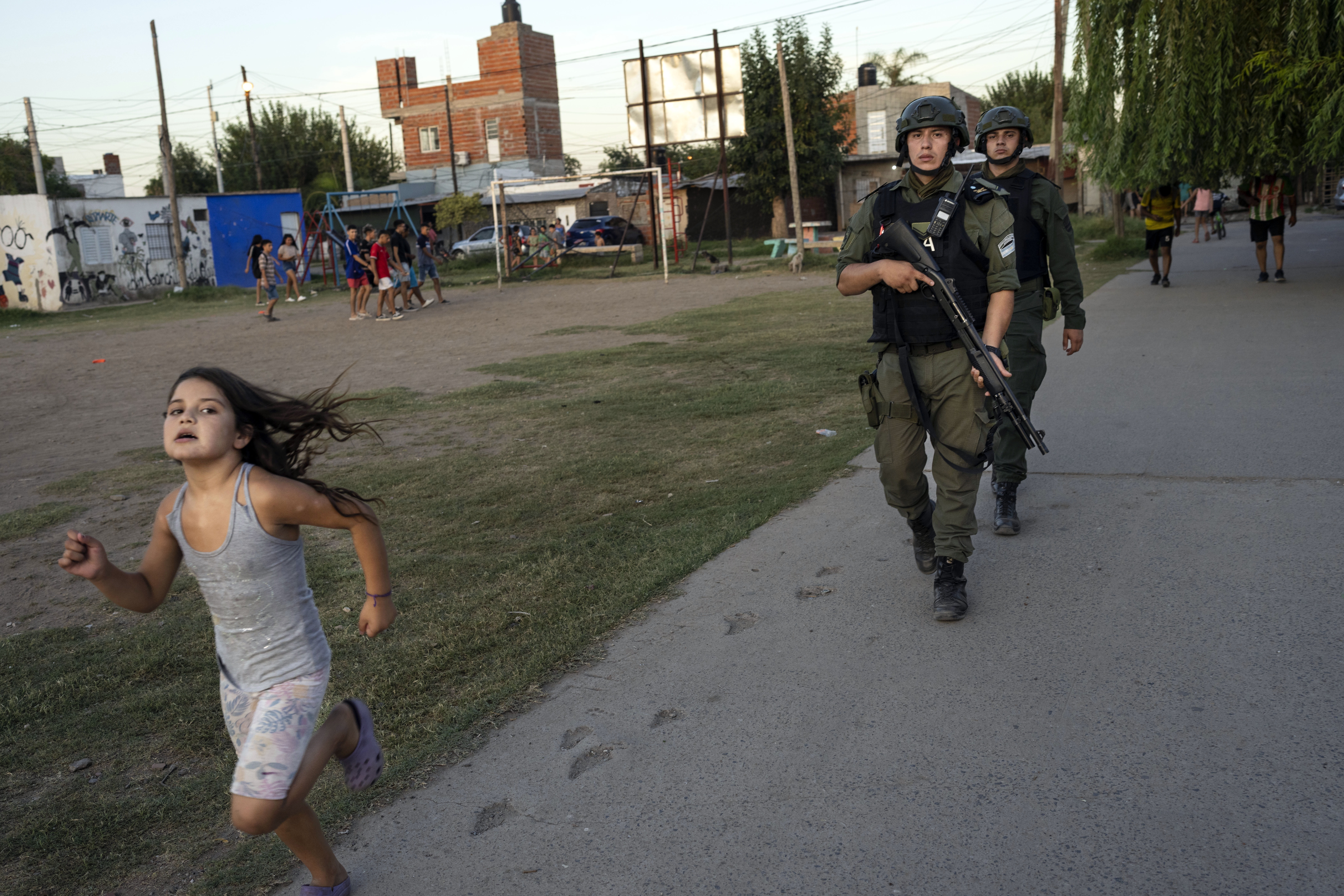 Una niña corre mientras agentes de la policía fronteriza patrullan en el vecindarios de Los Pumitas, donde Máximo Jerez, de 11 años, fue asesinado en la madrugada del domingo cuando al menos un pistolero atacó una fiesta de cumpleaños, en Rosario, Argentina, el jueves 9 de marzo de 2023. Horas después del entierro, residentes en un barrio del norte de Rosario donde supuestamente vivía el agresor, atacaron y destrozaron su vivienda. (AP Foto/Rodrigo Abd)