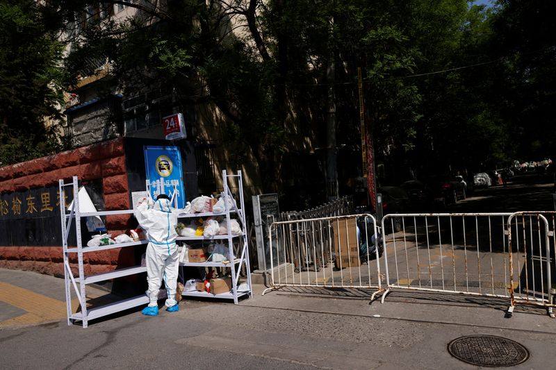 Una persona con traje de protección clasifica las entregas en un estante fuera de un área bajo confinamiento, durante la pandemia de COVID-19, en Pekín, China, 2 de mayo de 2022. REUTERS/Carlos García Rawlins