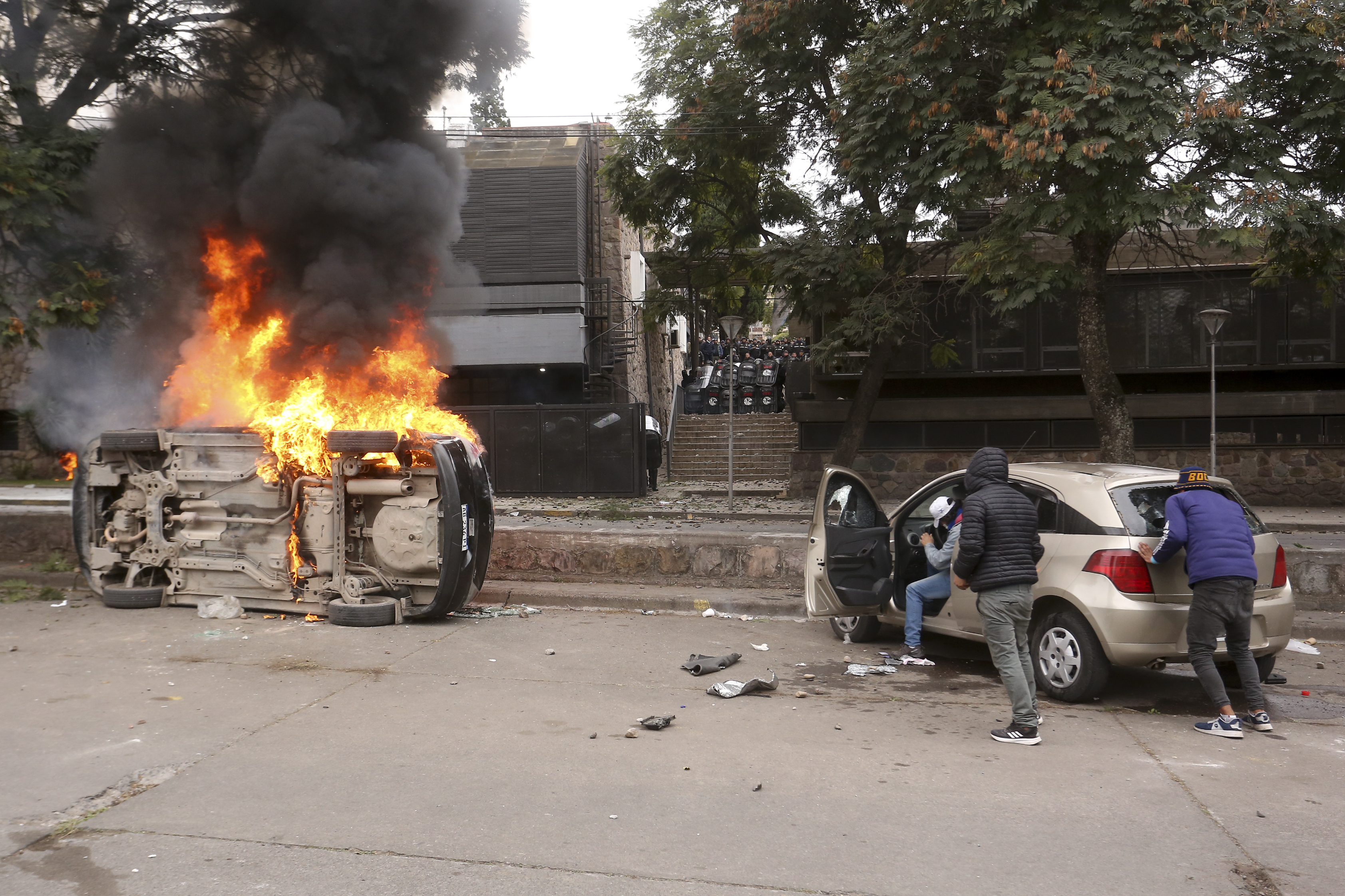 Los manifestantes se acercan a un automóvil mientras otro arde volteado durante una manifestación en San Salvador de Jujuy (Foto AP/Juan Burgos)