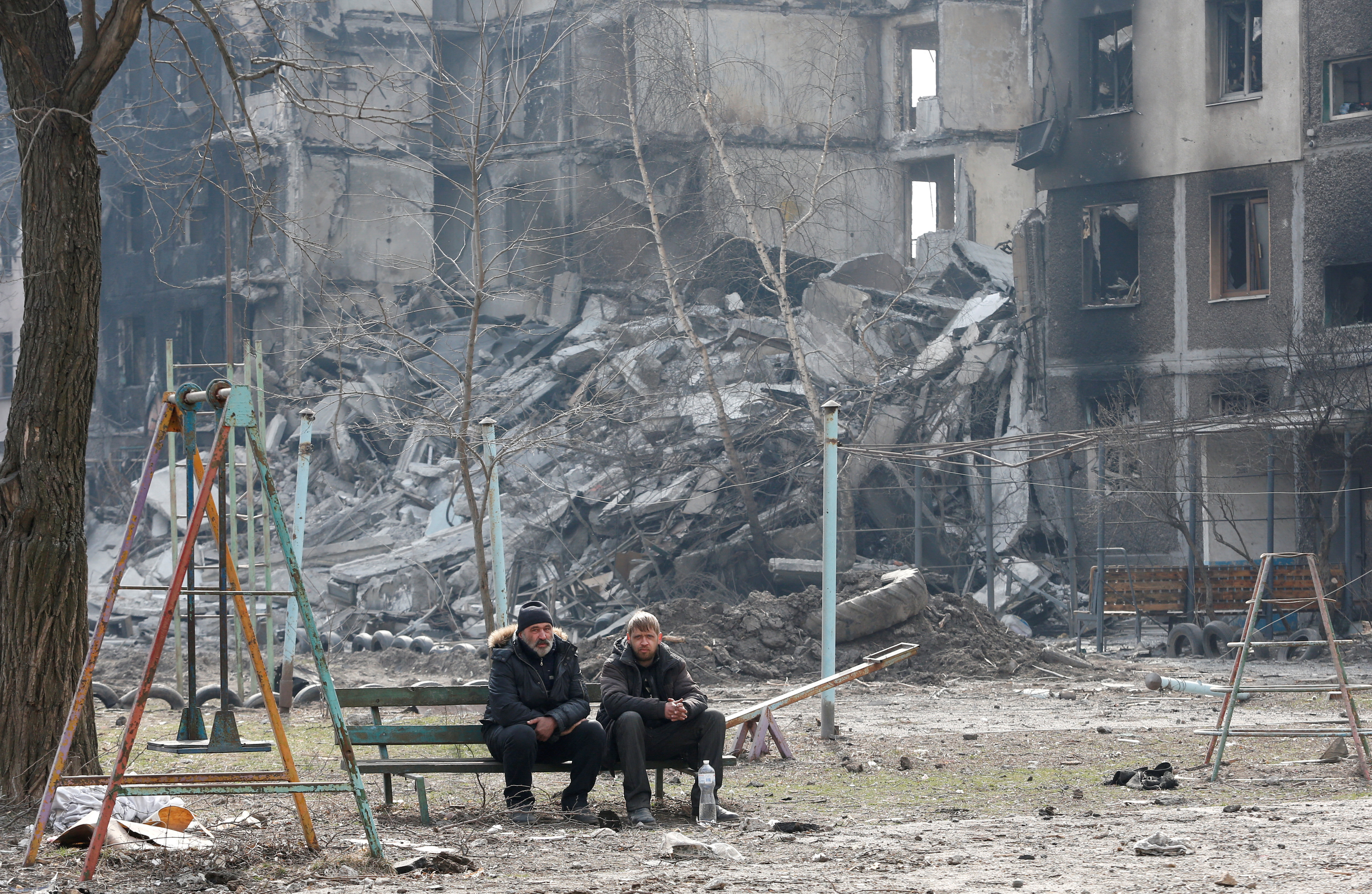 Los lugareños se sientan en bancos cerca de edificios de apartamentos destruidos por el conflicto ucraniano-ruso en la sitiada ciudad portuaria del sur de Mariupol, Ucrania, 25 de marzo de 2022. REUTERS/Alexander Ermochenko IMÁGENES TPX DEL DÍA