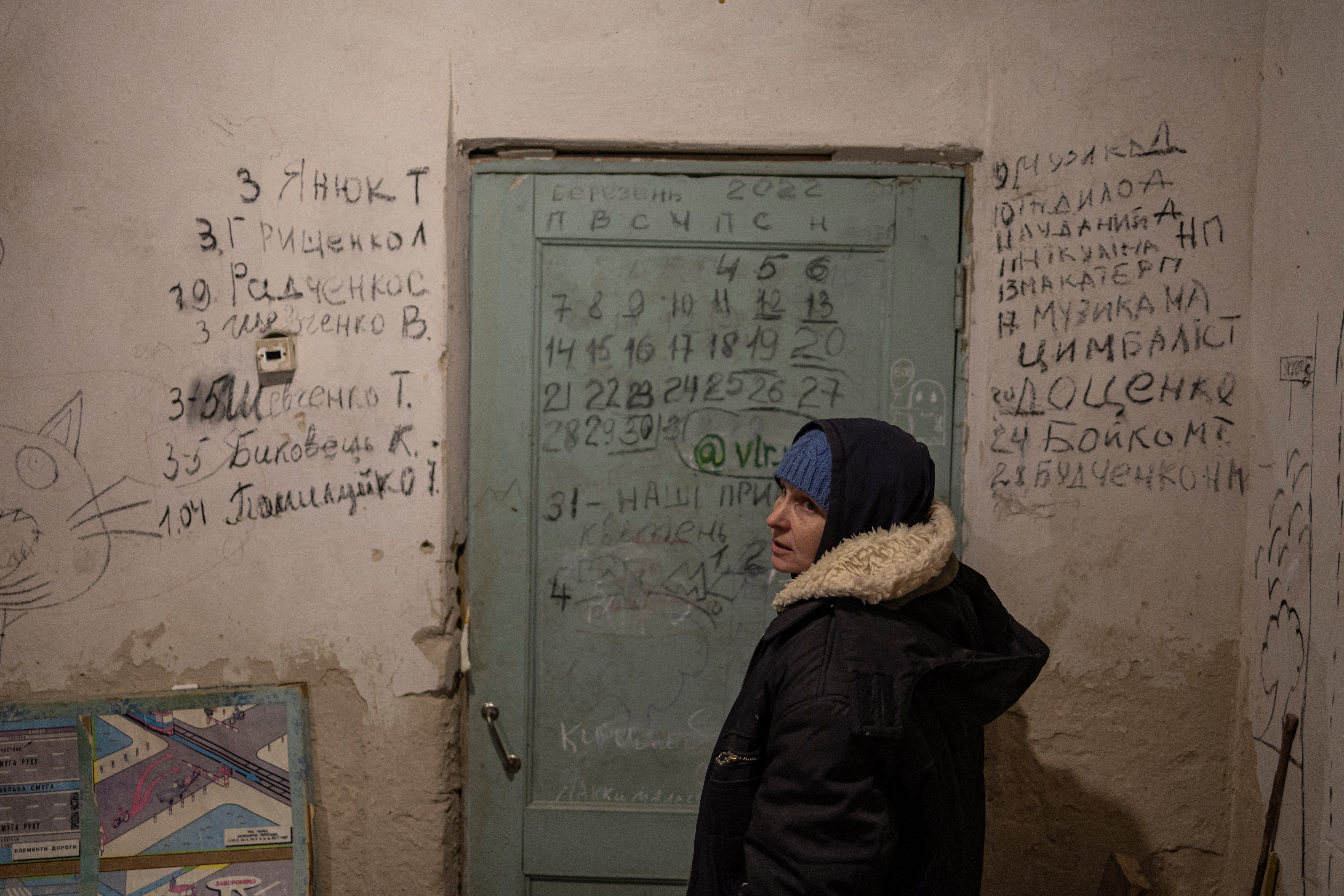Halyna Tolochina está frente a una pared en la que se colocó un calendario y los nombres de las personas que fueron muriendo den tro del sótano en el que estaban confinadas. a la izquierda de la puerta, las personas asesinadas por las tropas rusas, a la derecha, las de las que murieron por causas "naturales" debido al encierro y sus patologías previas. El primero de ellos, Dmytro Muzyka, falleció el 9 de marzo REUTERS/Marko Djurica