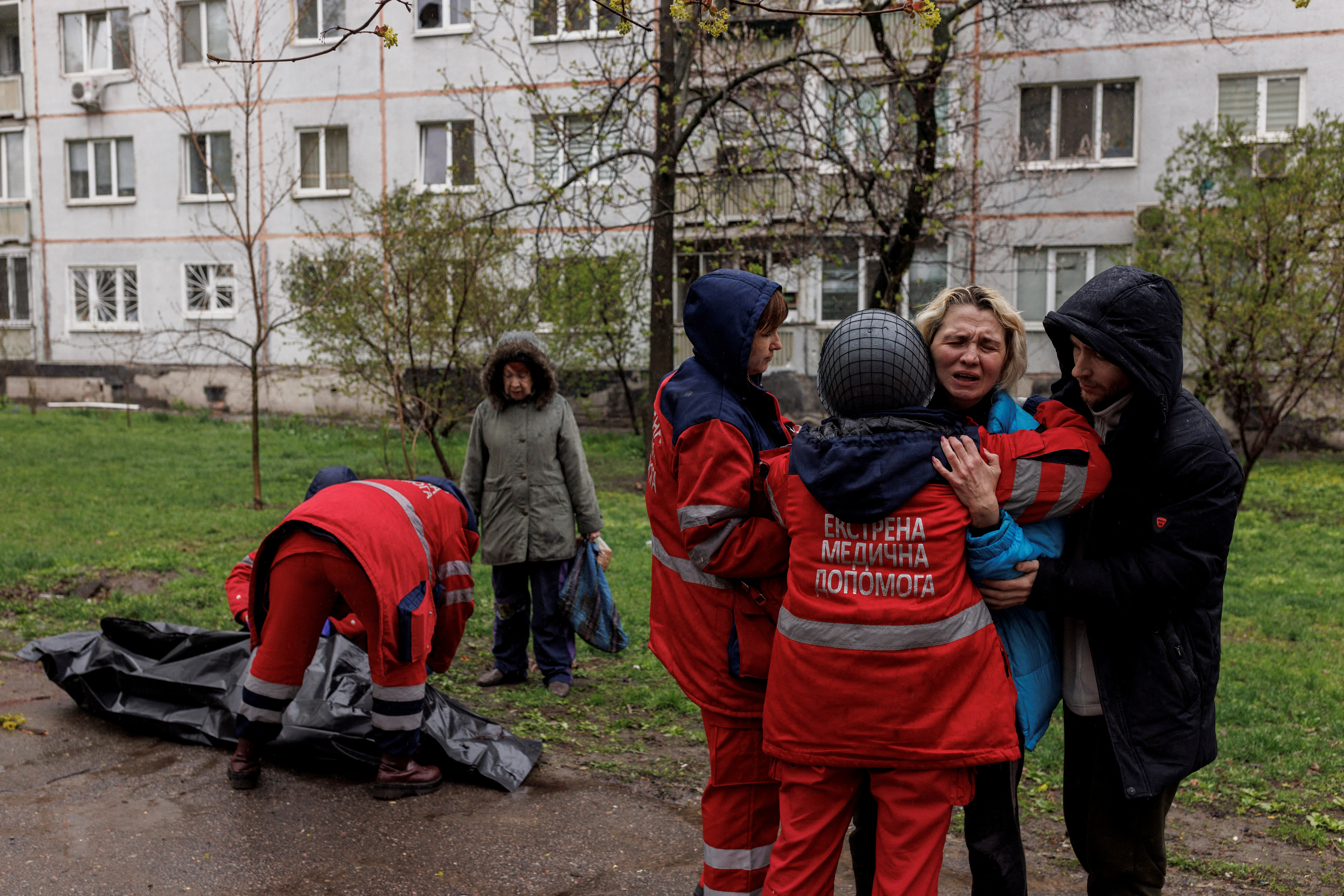 Yana Bachik mendapat penghiburan dari pasangannya Yevgeny Vlasenko dan penyelamat saat petugas medis mengambil jenazah ayahnya, Viktor Gubarev, 79, yang tewas dalam pemboman selama invasi Rusia ke Ukraina di Kharkiv (Reuters / Alexis Konstantinidis)