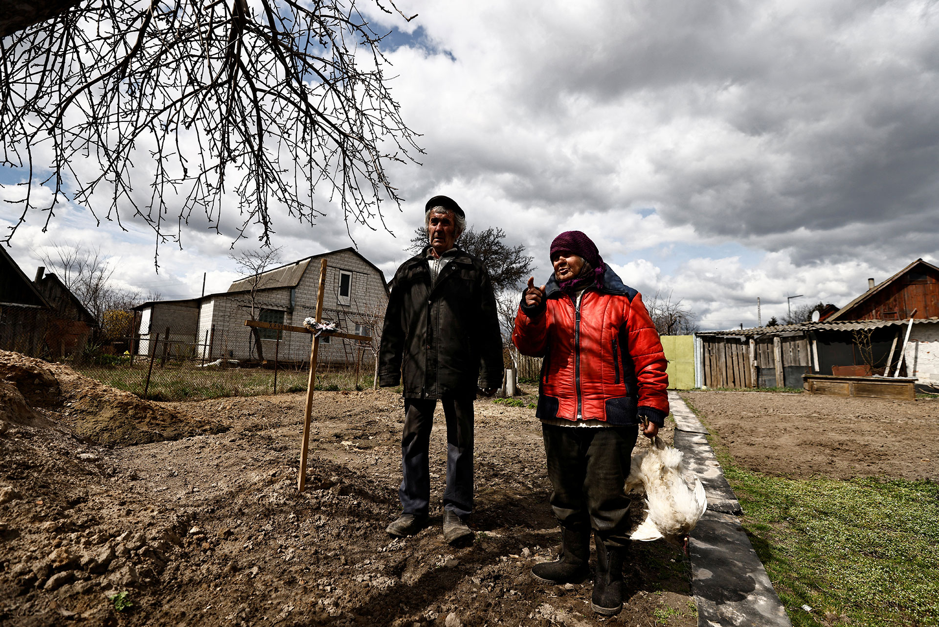 Zinaida Makishaiva, de 82 años, que sobrevivió a la ocupación rusa, se encuentra con Volodymyr Maksuta, de 62, junto a la tumba de su vecino, Yurii Ostapchuk


