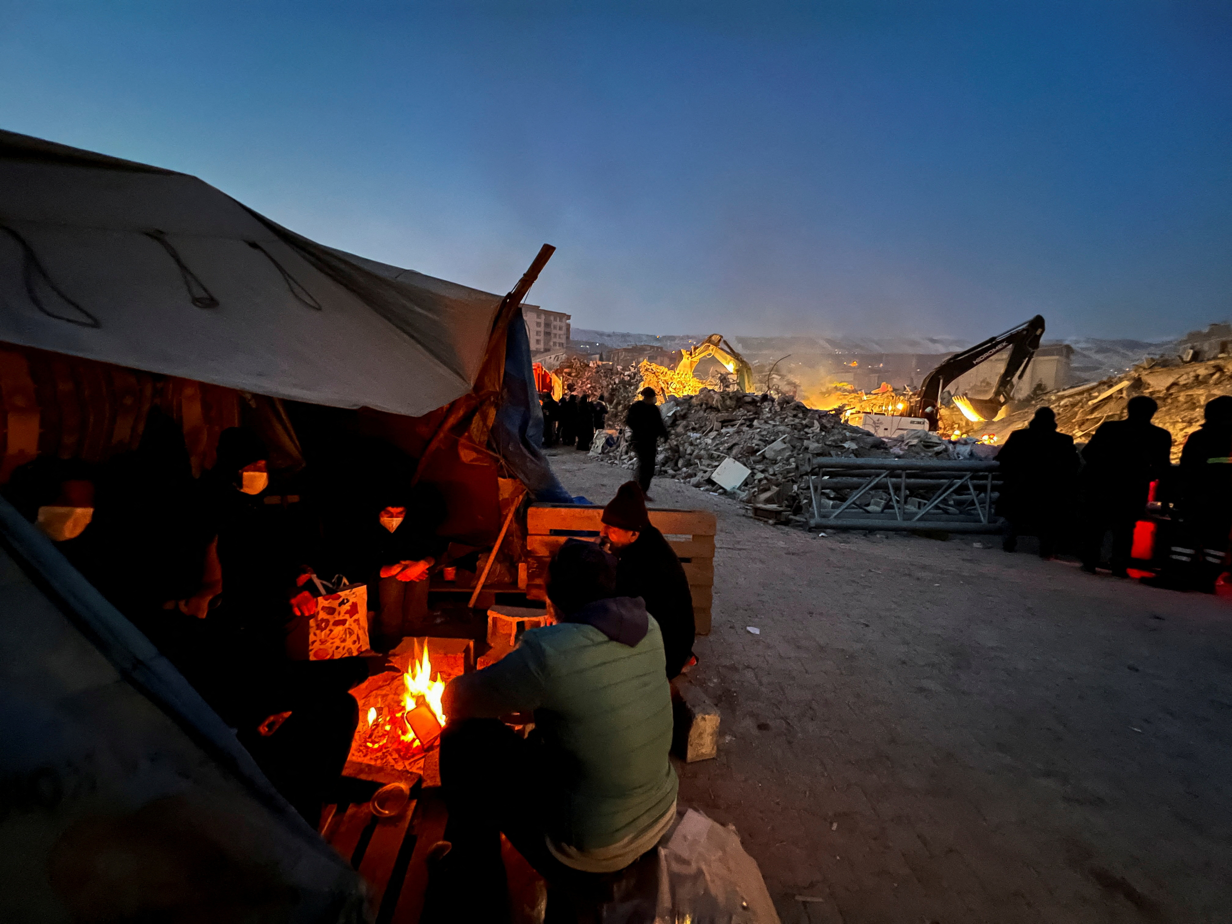La gente se sienta alrededor de un fuego cerca del lugar de un edificio derrumbado, mientras continúa la búsqueda de supervivientes, tras un terremoto en Kahramanmaras, Turquía 9 de febrero 2023. REUTERS/Suhaib Salem