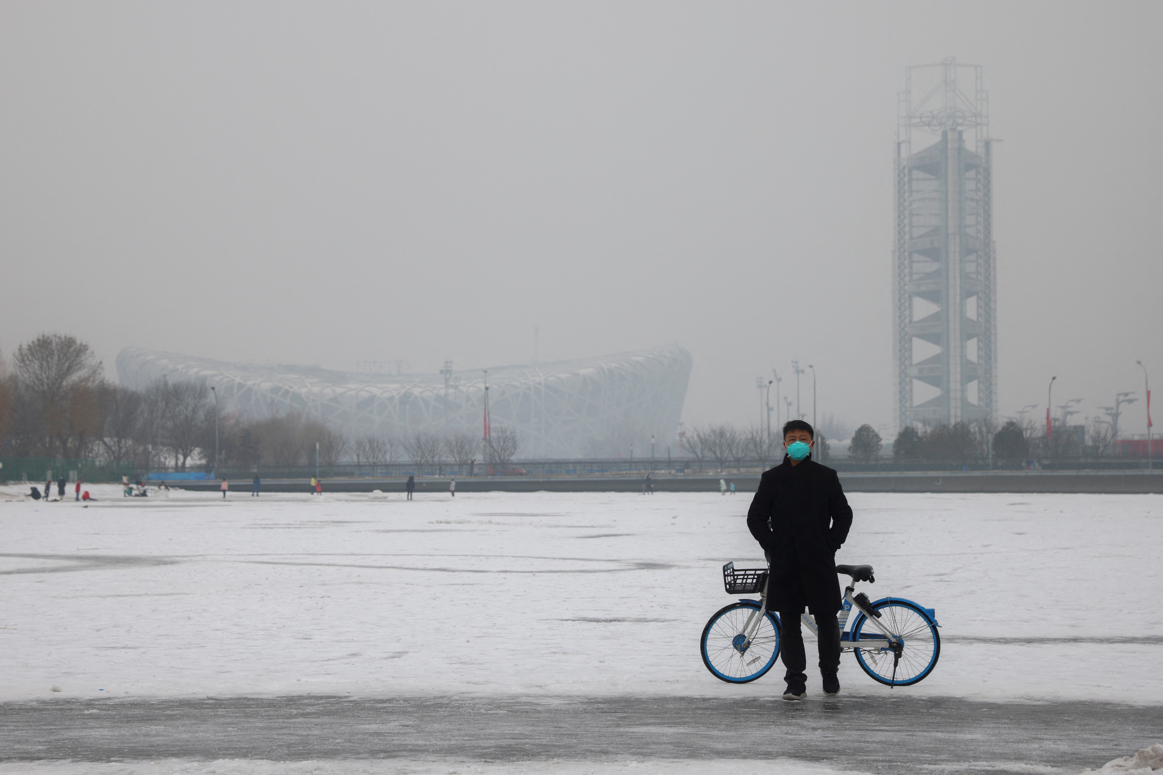 A man wearing a face mask stands on a frozen canal near the closed loop "bubble" surrounding venues of the Beijing 2022 Winter Olympics on a hazy day in Beijing, China, January 24, 2022.   REUTERS/Thomas Peter