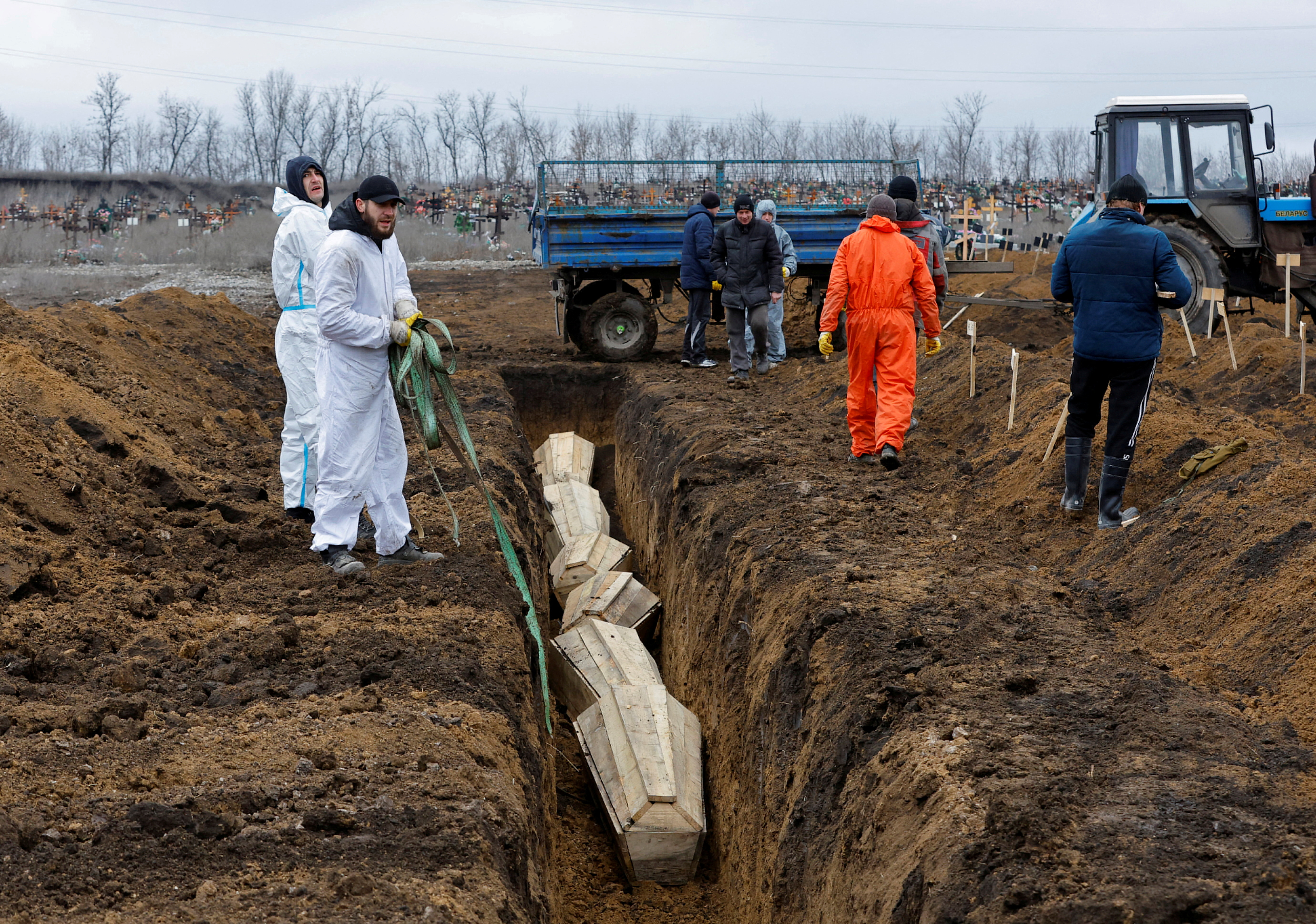 Trabajadores bajan ataúdes a una fosa común durante un entierro en un cementerio en el asentamiento de Staryi Krym a las afueras de Mariupol, Ucrania controlada por Rusia, 4 de febrero de 2023. (REUTERS/Alexander Ermochenko/Fotografía de archivo)