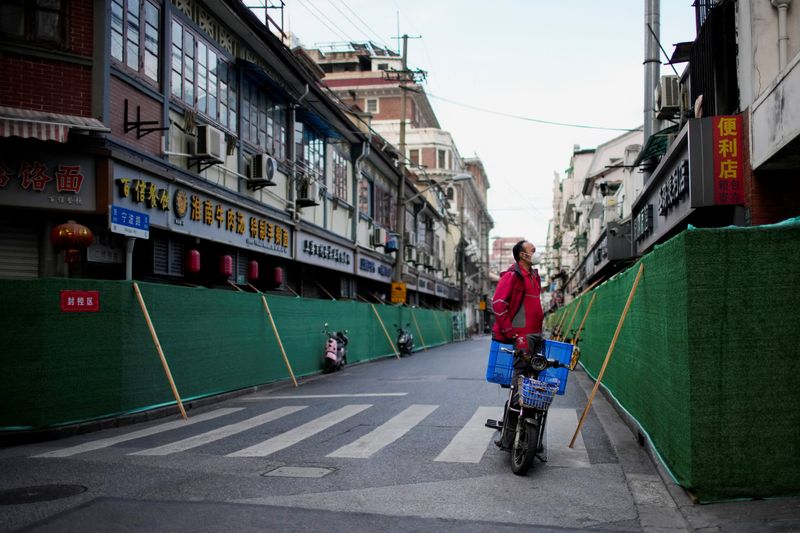 Un repartidor a domicilio con mascarilla en una motocicleta mira por encima de una barrera que rodea un área residencial durante el confinamiento por la COVID-19 en Shanghái, China, el 9 de mayo de 2022. REUTERS/Aly Song