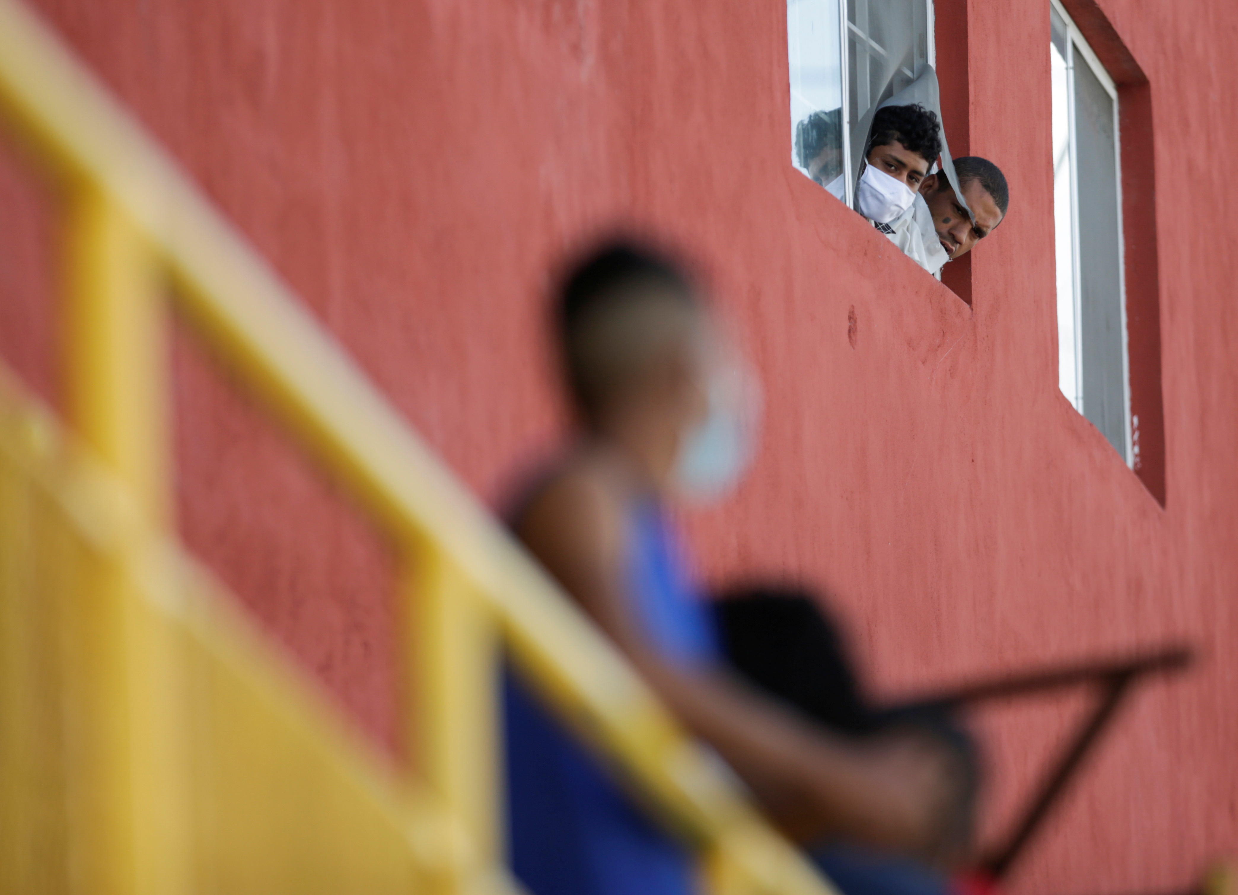 Los migrantes miran la calle desde una ventana en el refugio de migrantes