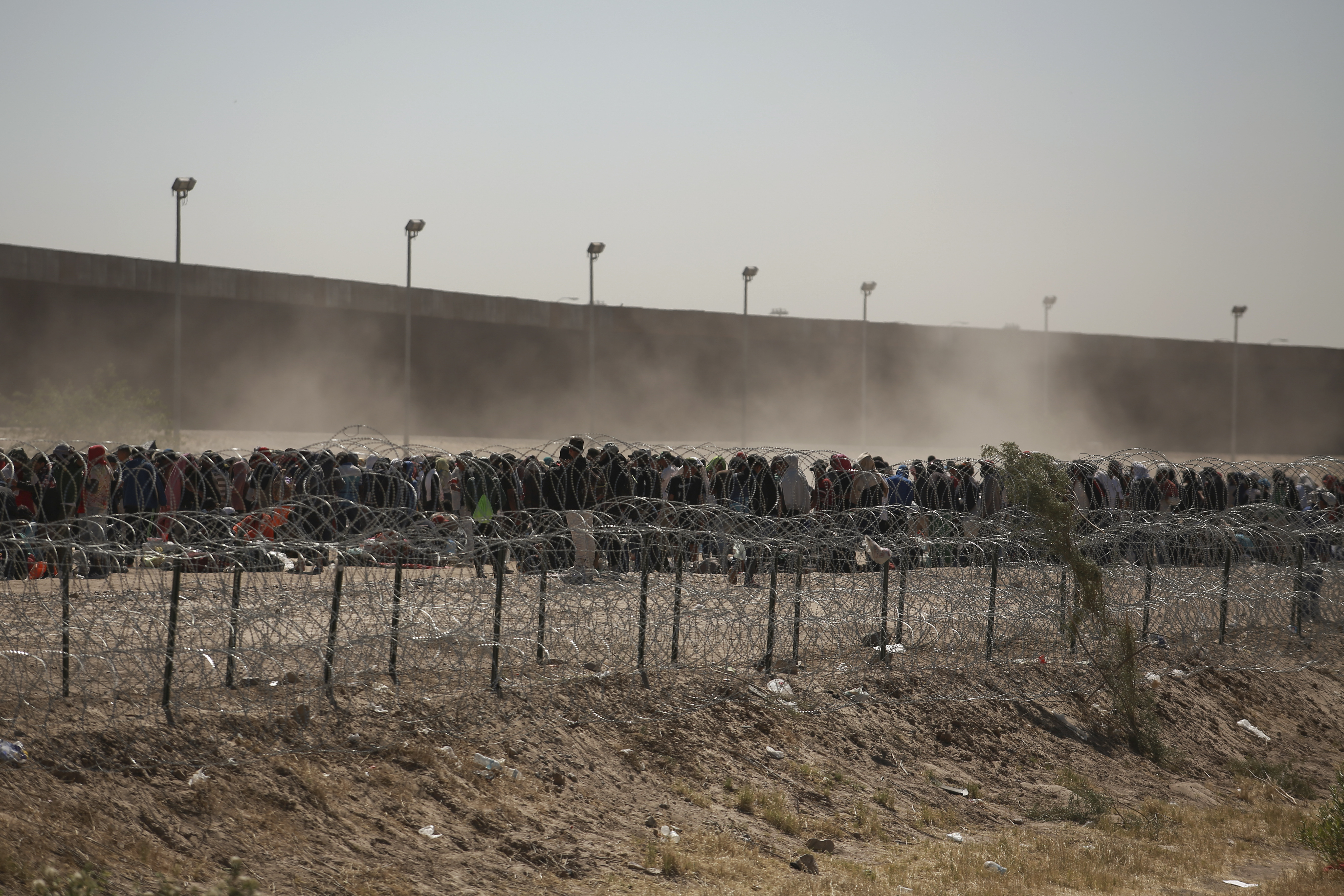 Migrants line up between a barbed wire barrier and the US-Mexico border wall, as seen from Ciudad Juárez, Mexico, on May 9, 2023. Migrants were rushing across the border before restrictions on asylum expired. imposed by the United States in connection with the pandemic, a change that threatens to put a historic burden on the country's battered immigration system.  (AP Photo/Christian Chavez)