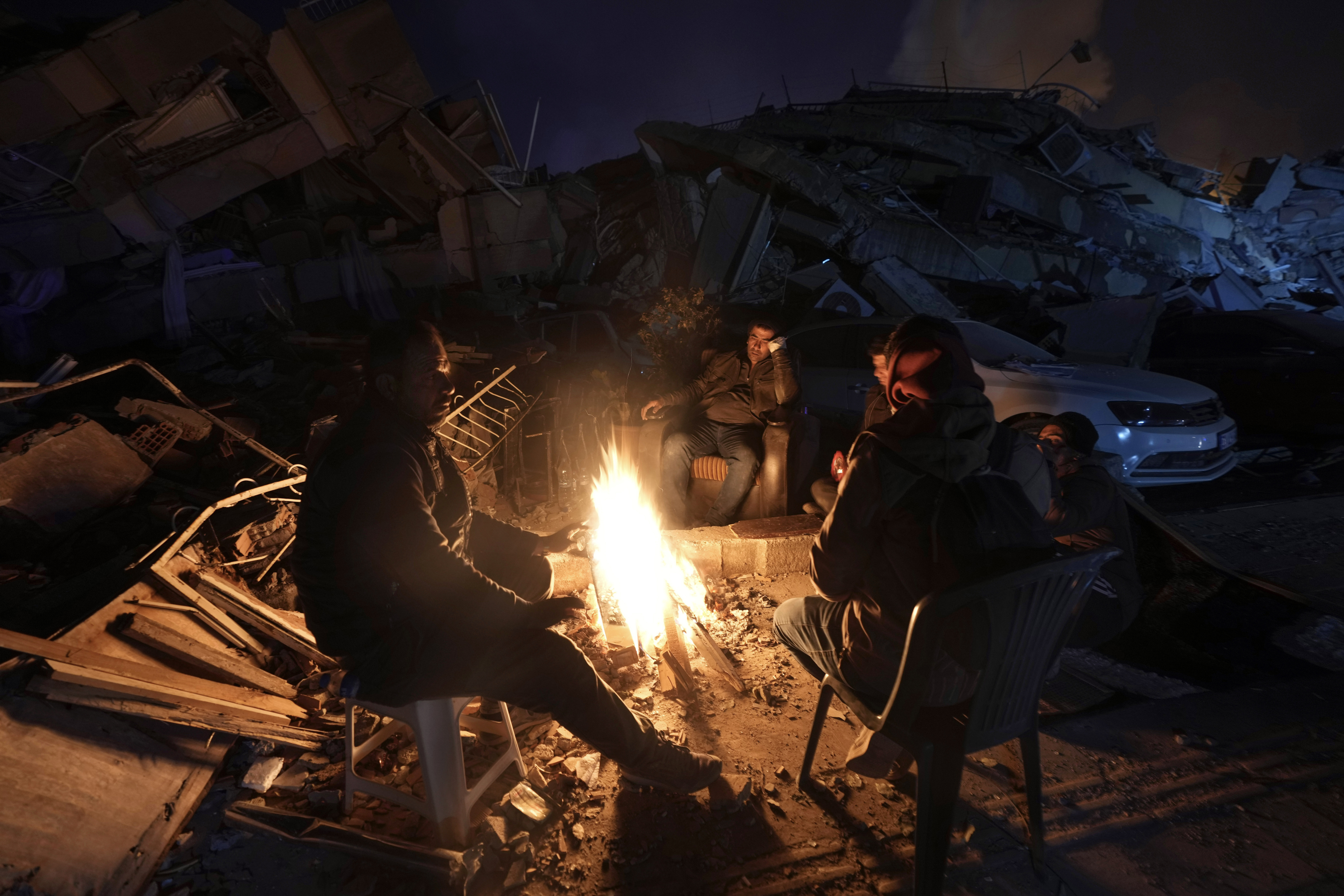 People warm up around a bonfire in front of buildings destroyed by a powerful earthquake, in Antakya, southern Turkey, on February 8, 2023. (AP Photo/Khalil Hamra)