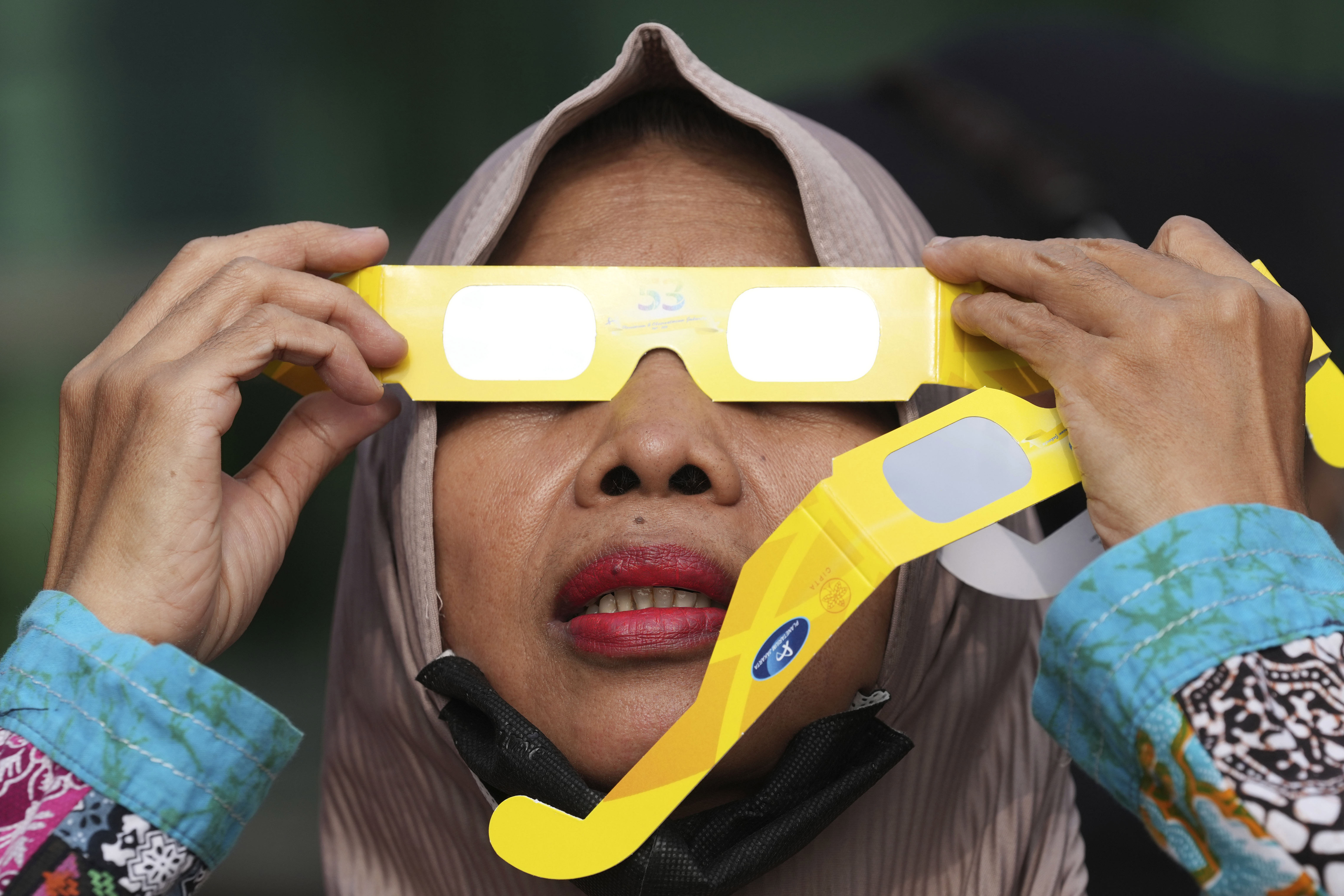 Una mujer utiliza gafas protectoras para ver un eclipse solar en Yakarta, Indonesia, el jueves 20 de abril de 2023. Los pocos afortunados en su ruta o bien vieron la oscuridad de un eclipse total o el “anillo de fuego” cuando el sol asomaba tras la Luna. (AP Foto/Tatan Syuflana)