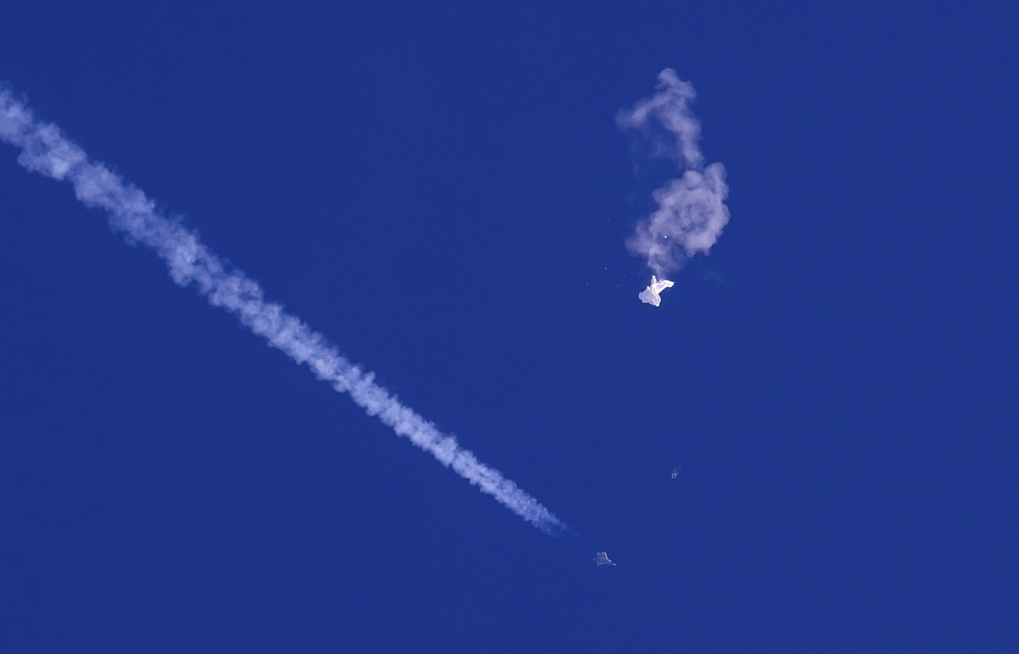 Fotografía de los restos del globo cayendo sobre el océano Atlántico frente a la costa de Carolina del Sur (arriba a la derecha), mientras abajo se observa un avión de combate y su estela, el sábado 4 de febrero de 2023. (Chad Fish vía AP)