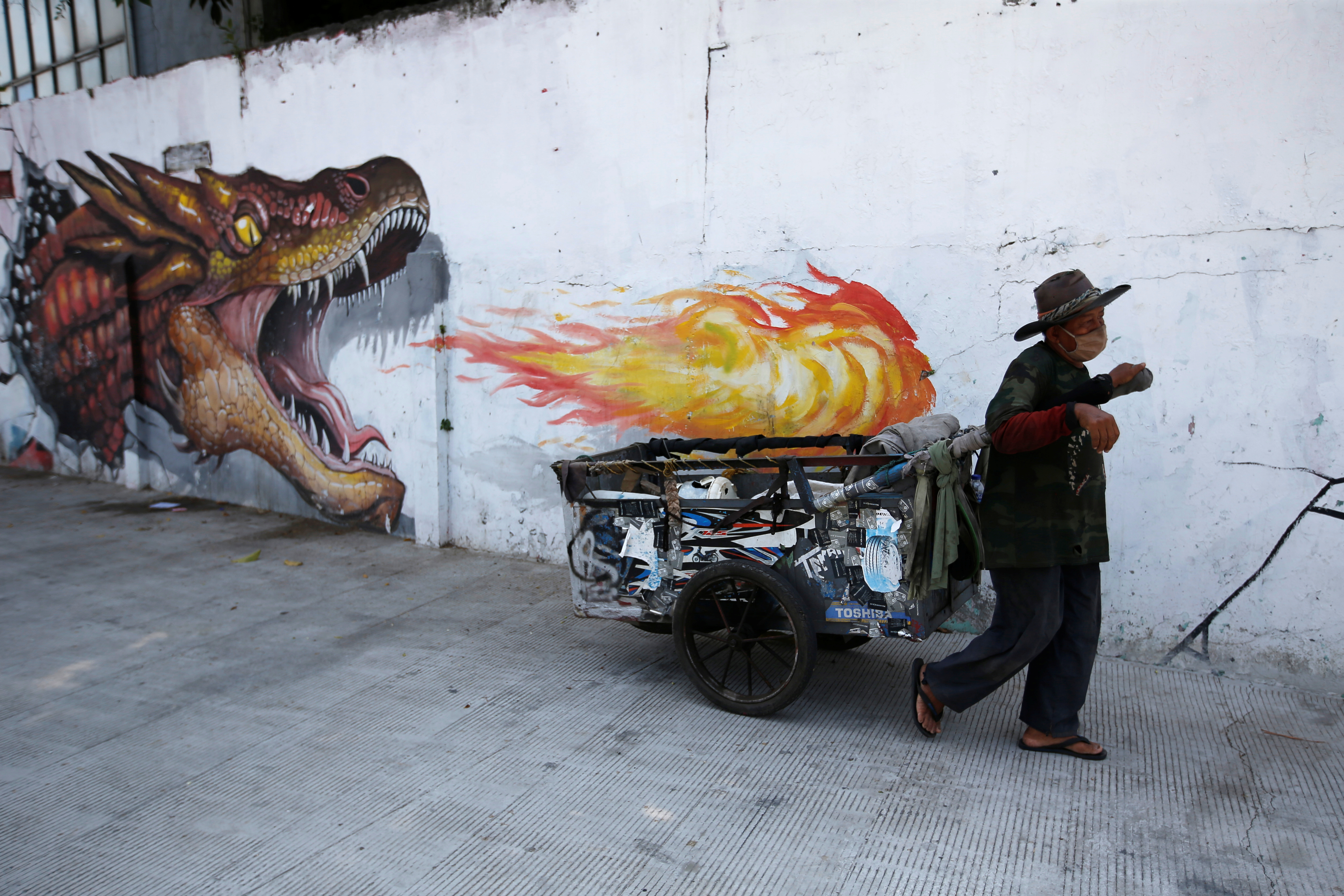 Un hombre con una máscara protectora tira de una carreta pasando por un mural mientras continúa el brote de la enfermedad coronavirus (COVID-19) en Yakarta, Indonesia, el 23 de agosto de 2020. REUTERS/Willy Kurniawan