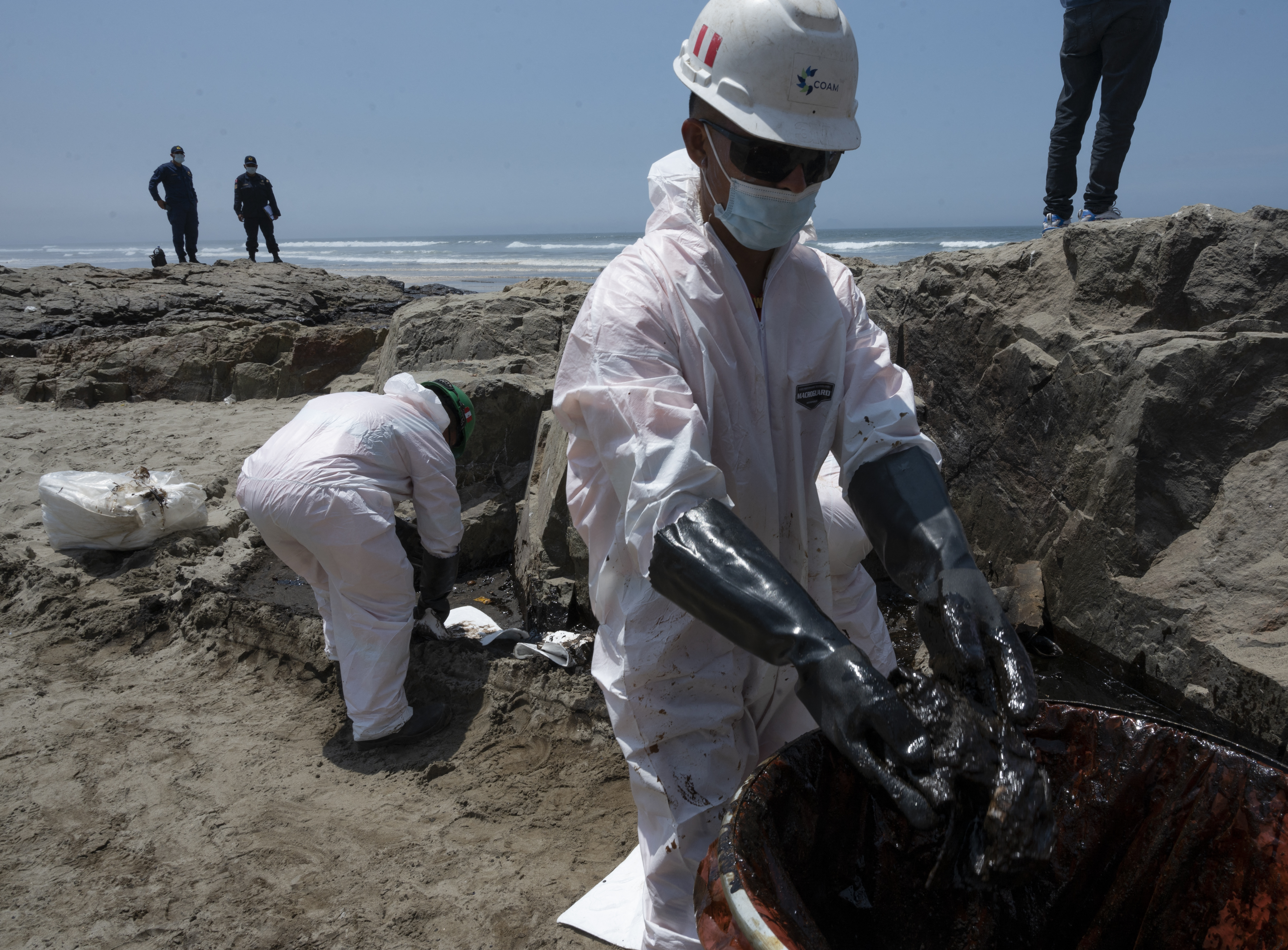 Cleaning crews work to remove oil from a beach in the Peruvian province of Callao on January 17, 2022, after a spill which occurred during the unloading process of the Italian-flagged tanker "Mare Doricum" at La Pampilla refinery caused by the abnormal waves recorded after the volcanic eruption in Tonga. - A massive volcanic eruption in Tonga triggered tsunami waves around the Pacific, with waves strong enough to drown two women in Peru, more than 10,000 kilometres (6,000 miles) away. (Photo by Cris BOURONCLE / AFP)