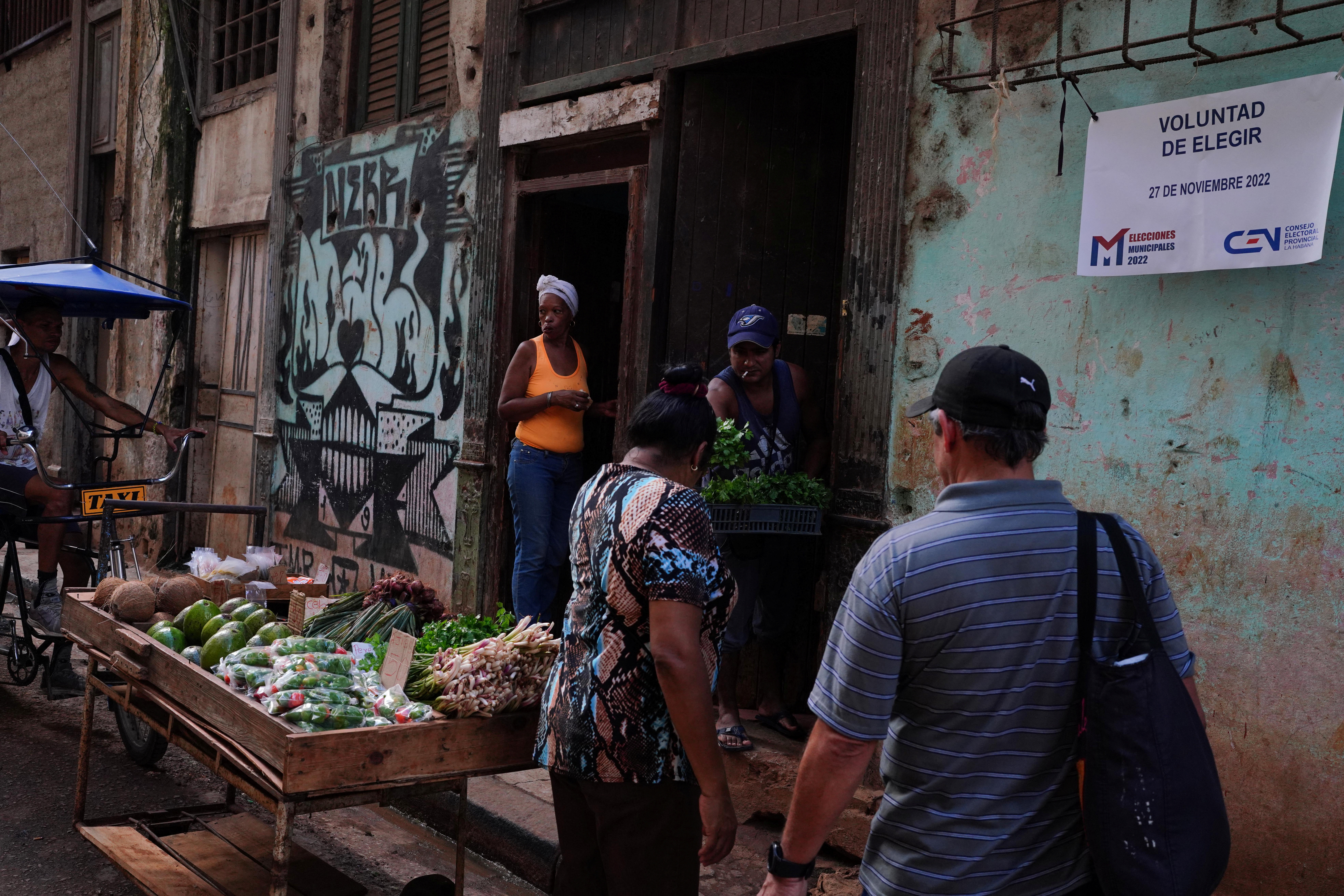 La gente compra verduras junto a un cartel que anuncia las elecciones municipales en el centro de La Habana, Cuba (Archivo/Reuters)