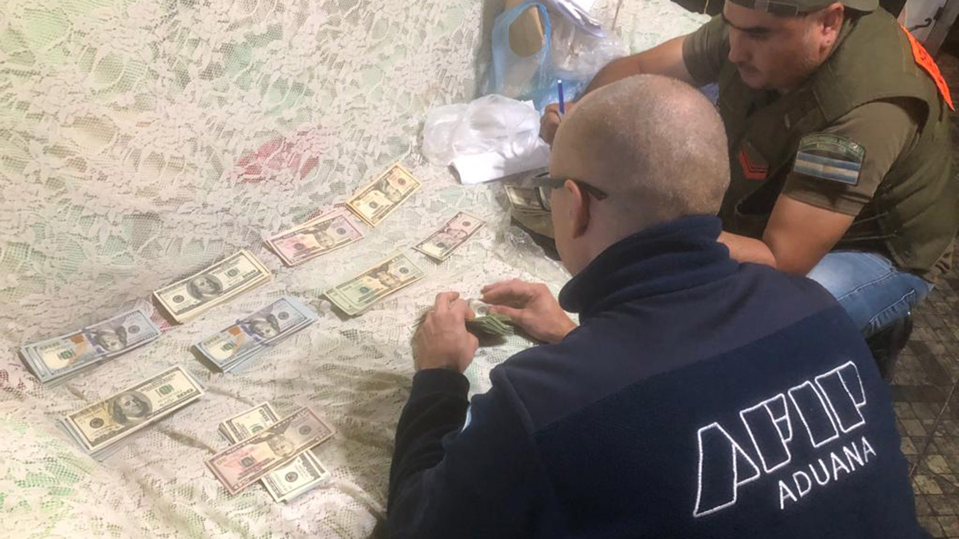 Agentes de Aduana cuentan dólares en un depósito en Jujuy en el que secuestraron vehículos, neumáticos y una máquina de contar billetes de una masiva operación de contrabando de cubiertas
