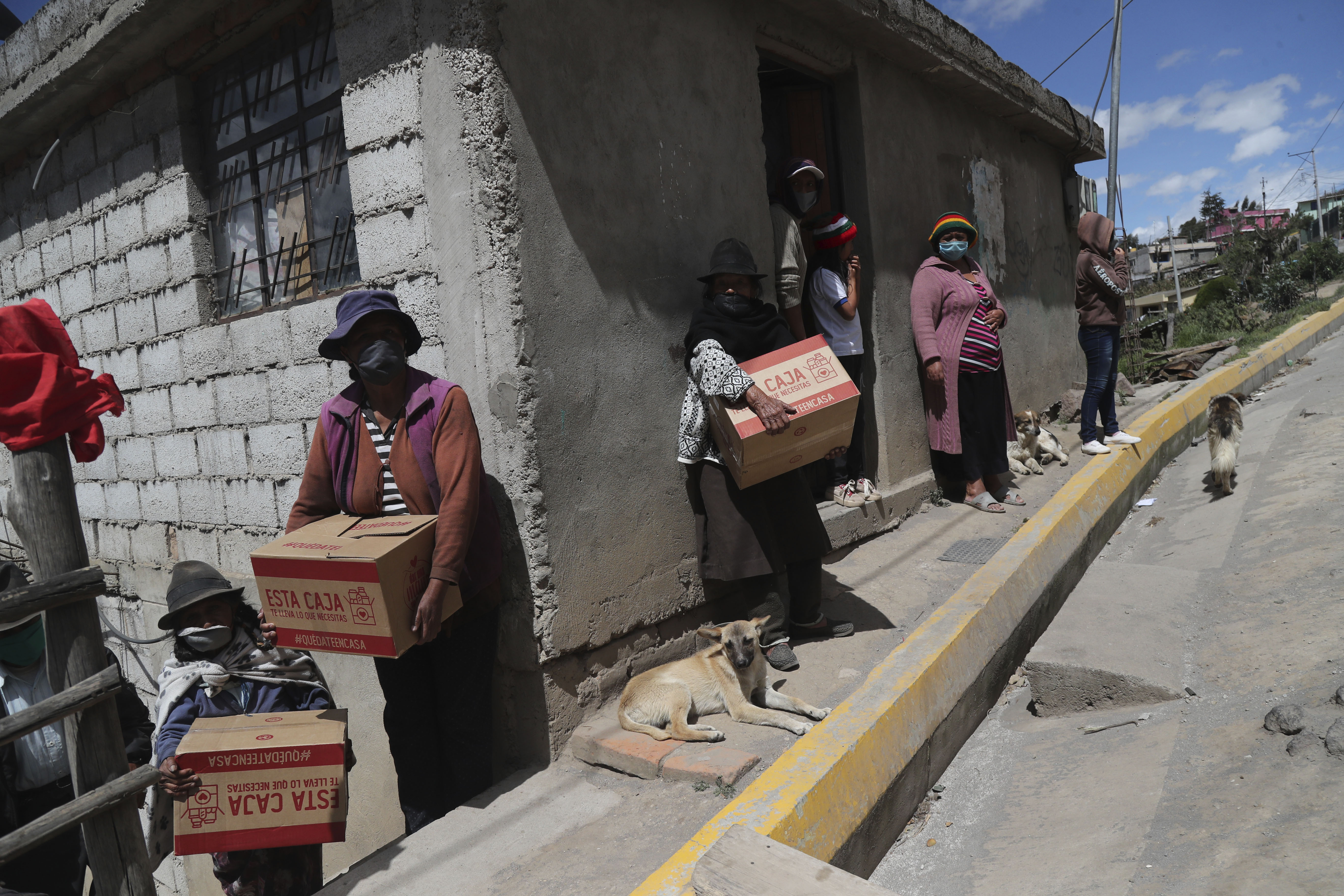 Vecinas con mascarilla sostienen cajas de alimentos distribuidas por el gobierno, durante una cuarentena para combatir la expansión del COVID-19 a las afueras de Quito, Ecuador, el miércoles 27 de mayo de 2020. En toda la región, se espera que casi 30 millones de personas más se vean en “situaciones de pobreza” y otros 16 millones en pobreza extrema, según las estimaciones de Naciones Unidas. (AP Foto/Dolores Ochoa)