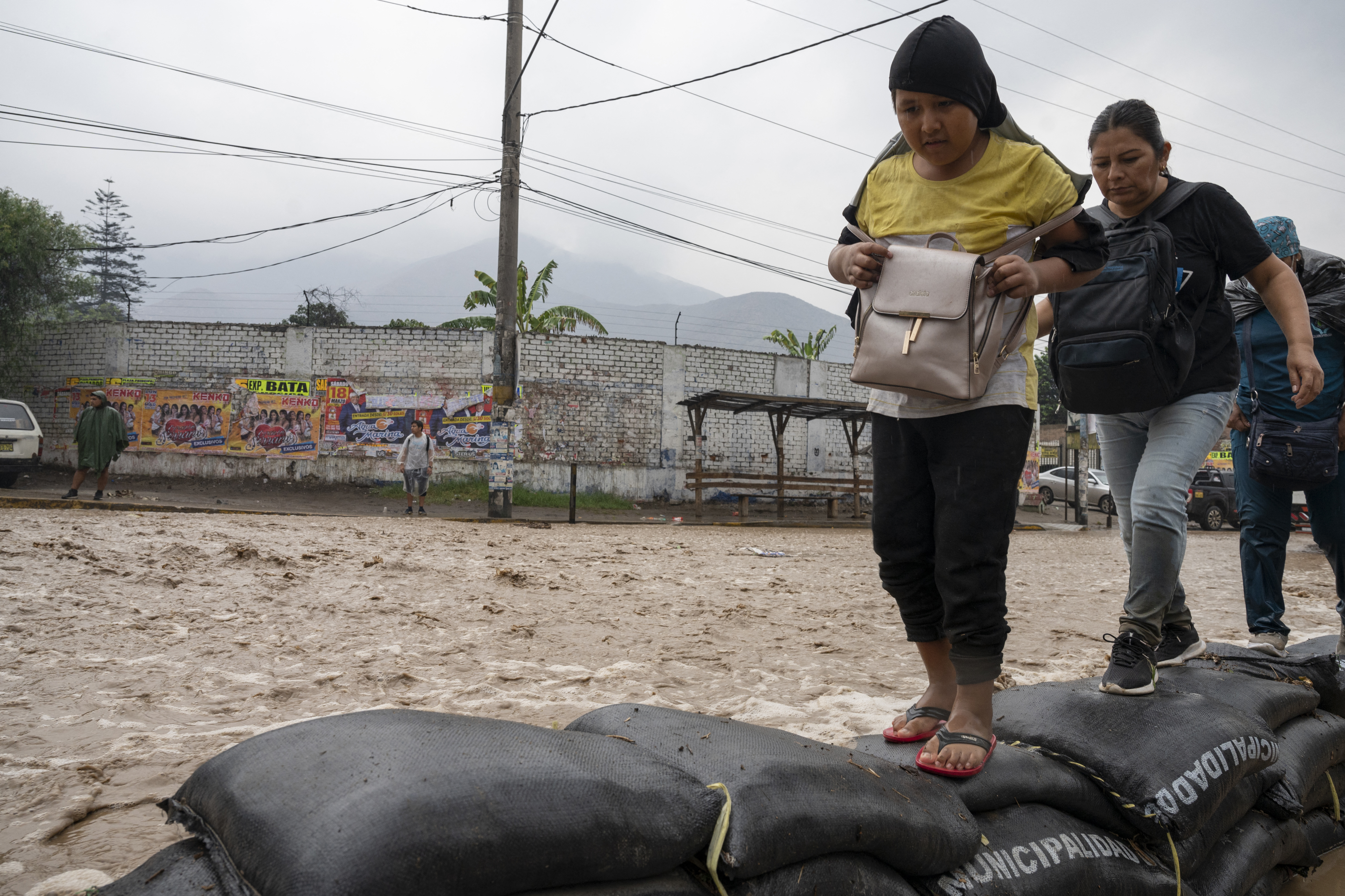 Las personas caminan a través del agua que inunda la principal vía de acceso desde Lima al interior del país  luego de las fuertes lluvias en Chaclacayo. (AFP)