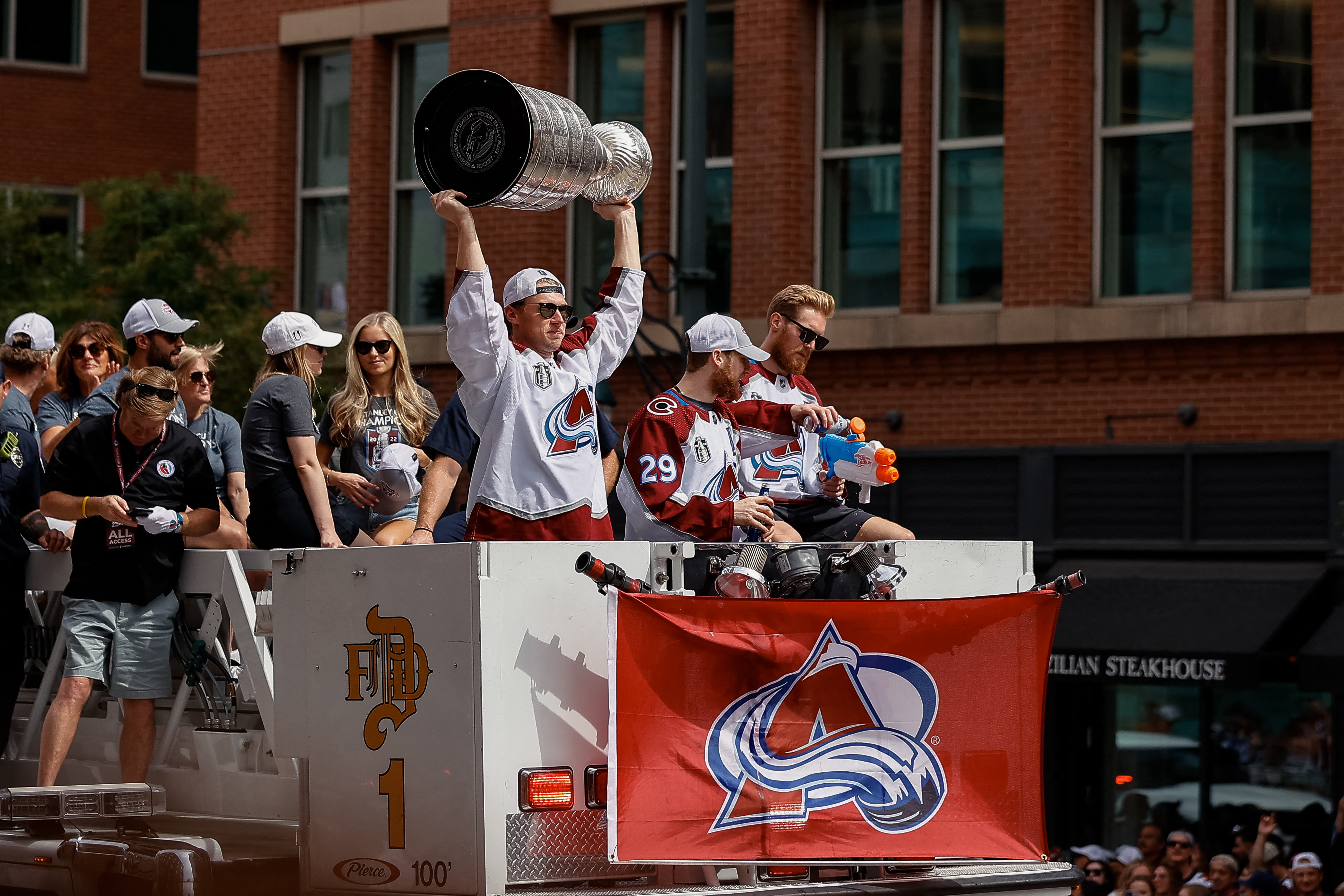 Jun 30, 2022; Denver, Colorado, USA; Colorado Avalanche player Erik Johnson lifts the Stanley Cup as teammate Nathan MacKinnon watches Gabriel Landsekog fills a squirt gun with water during the Stanley Cup celebration parade as it makes its way through downtown Denver towards Civic Center Park. Mandatory Credit: Isaiah J. Downing-USA TODAY Sports