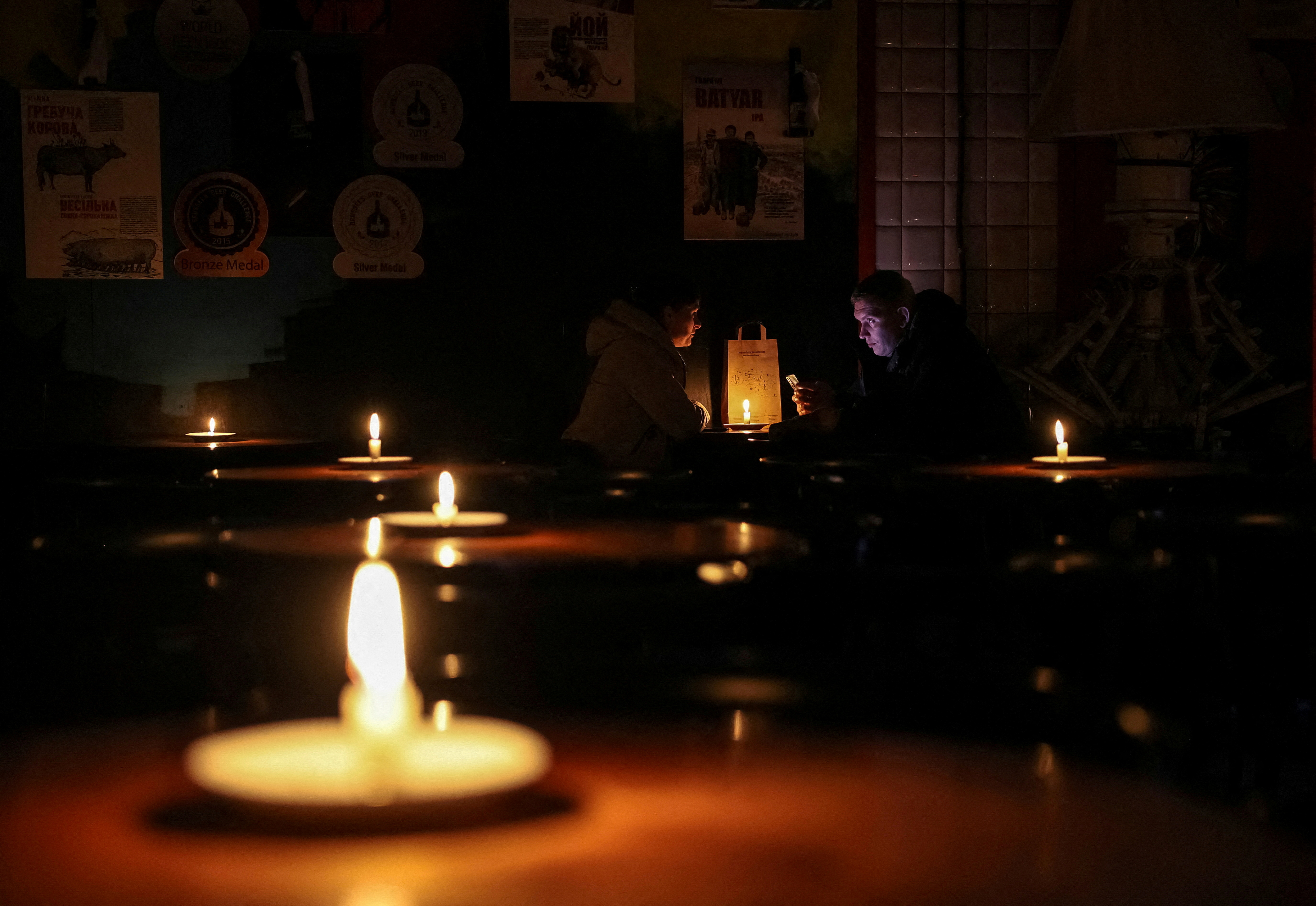 Un grupo de personas sentadas en un bar iluminado con velas durante un apagón después de que infraestructuras civiles críticas fueran alcanzadas por ataques de misiles rusos, en Lviv (REUTERS/Roman Baluk)