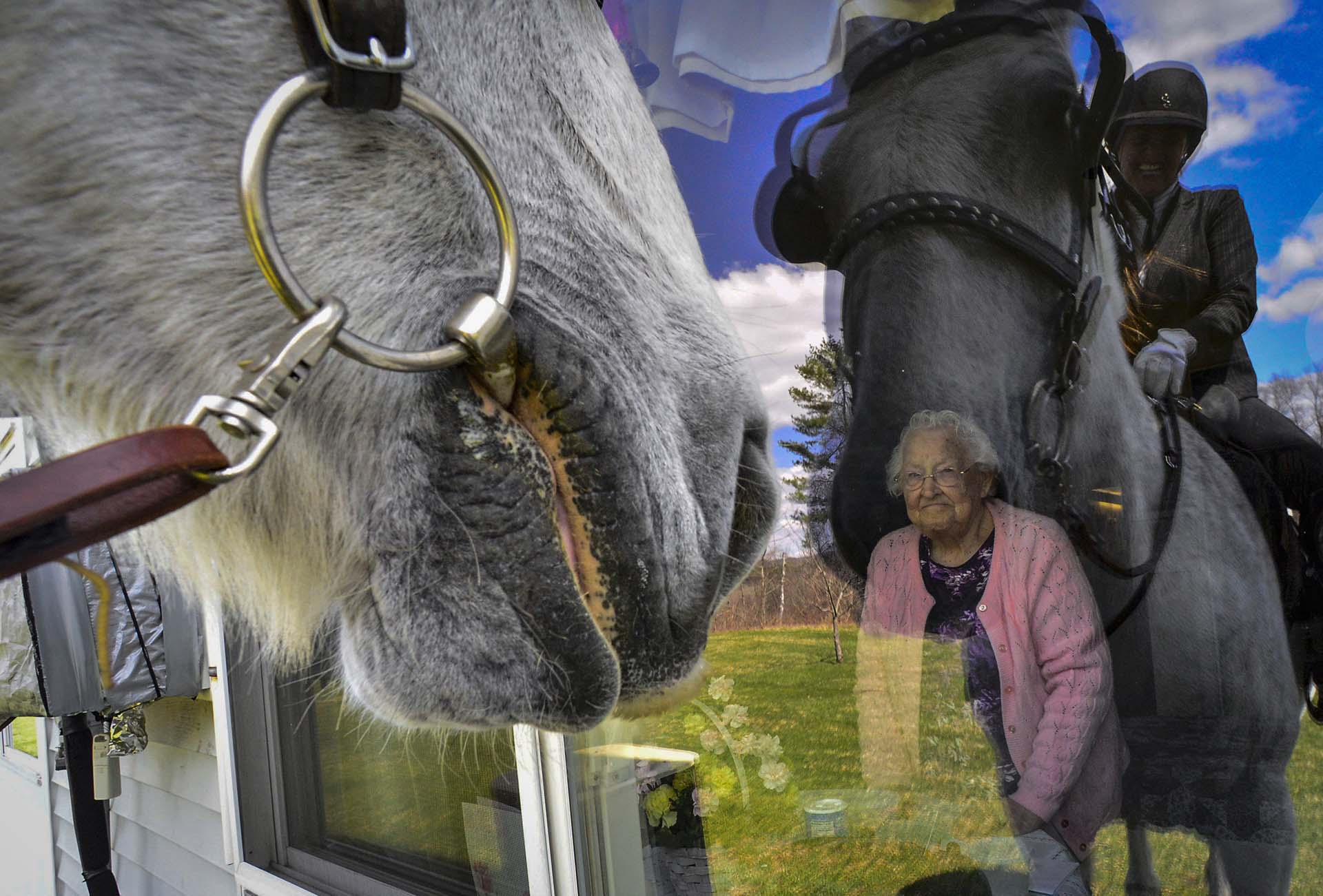 Una residente de un hogar para mayores en Vermont mira por la ventana mientras una mujer se acerca montando a un caballo (Kristopher Radder/The Brattleboro Reformer via AP)