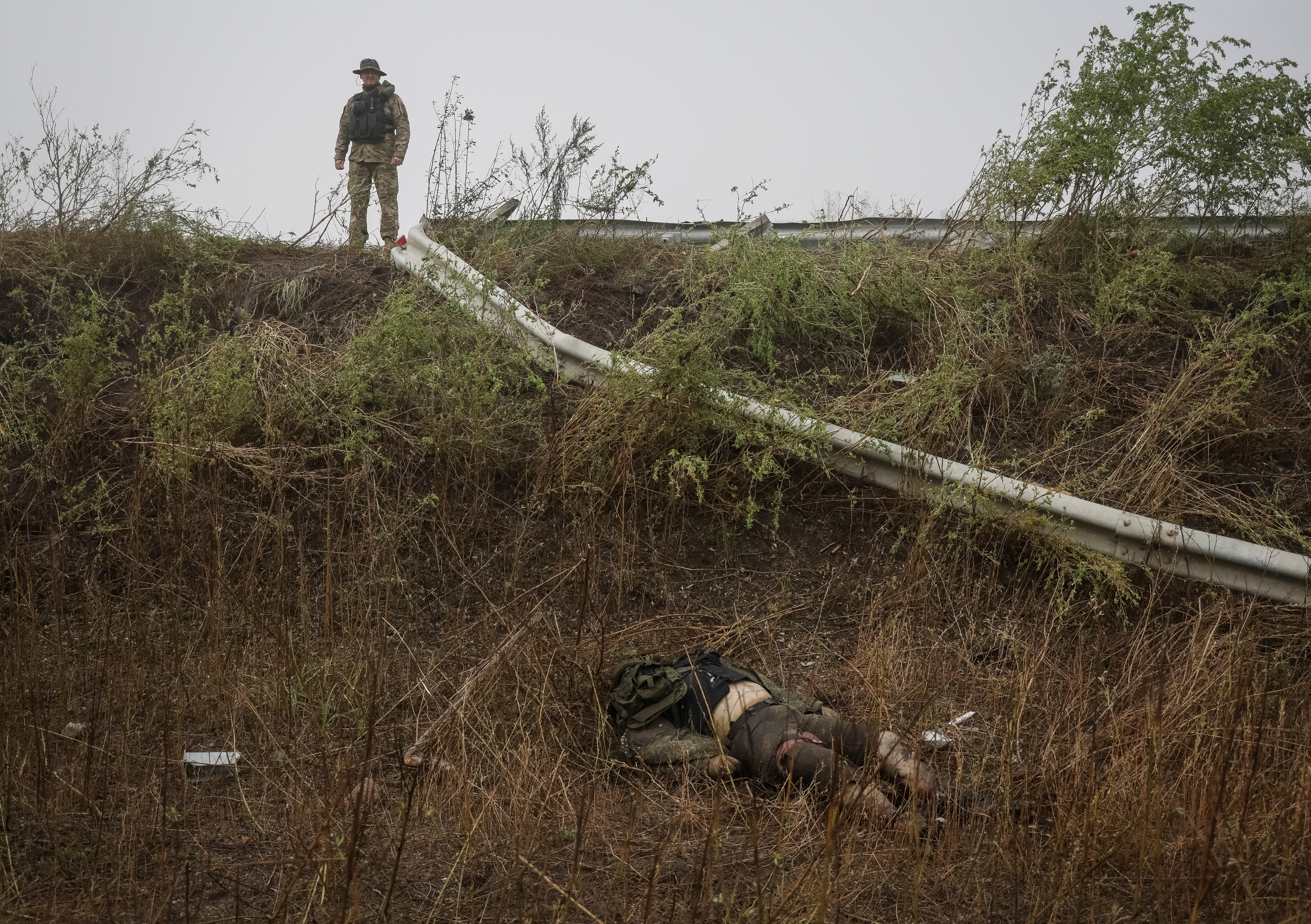 A Ukrainian soldier looks over the body of a Russian soldier near the town of Issyum, which was recently liberated by Ukraine's armed forces (Reuters).