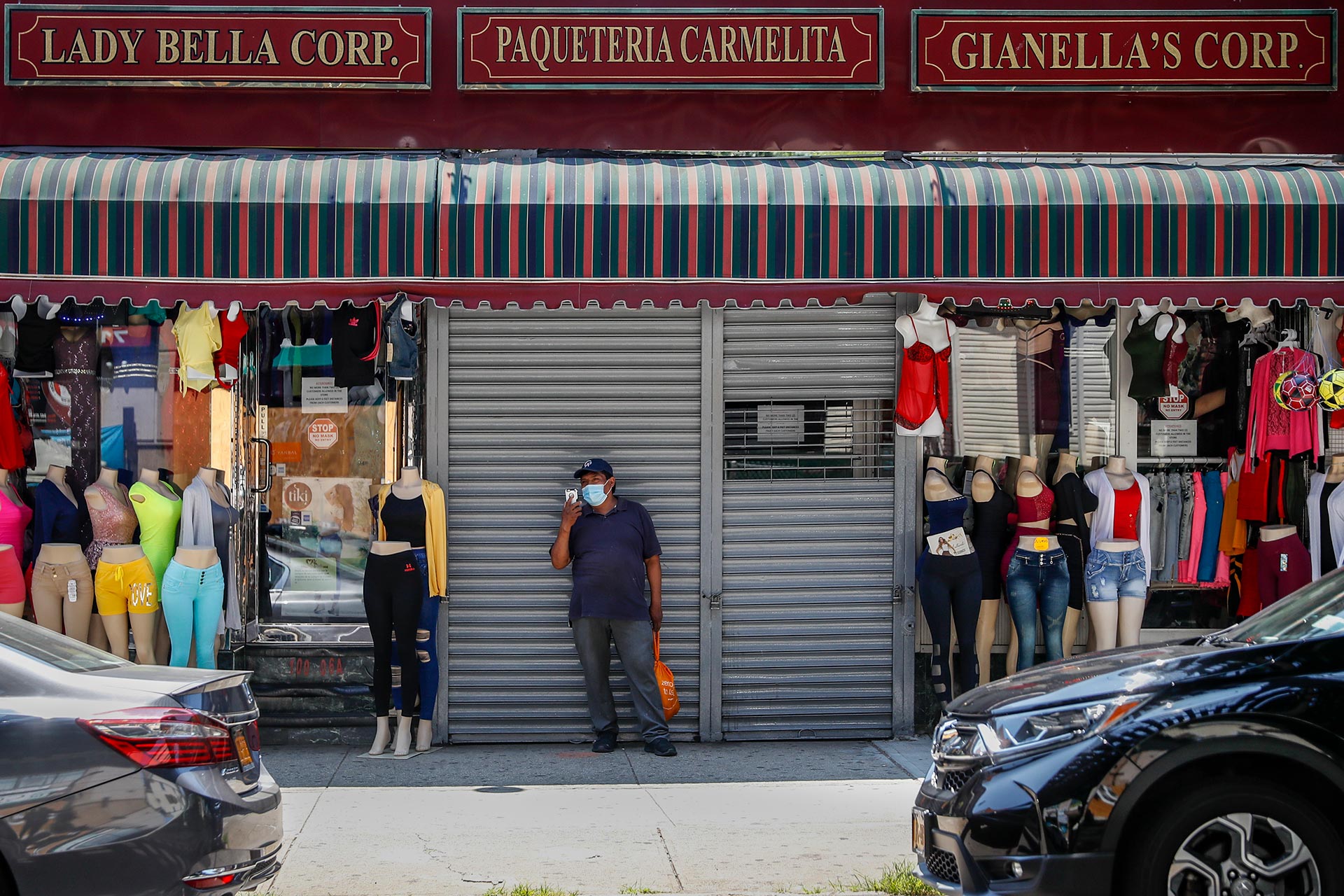 Un hombre, con mascarilla, delante de una tienda cerrada, en medio de otras dos de venta de ropa, en Queens, Nueva York. (Foto AP / John Minchillo)