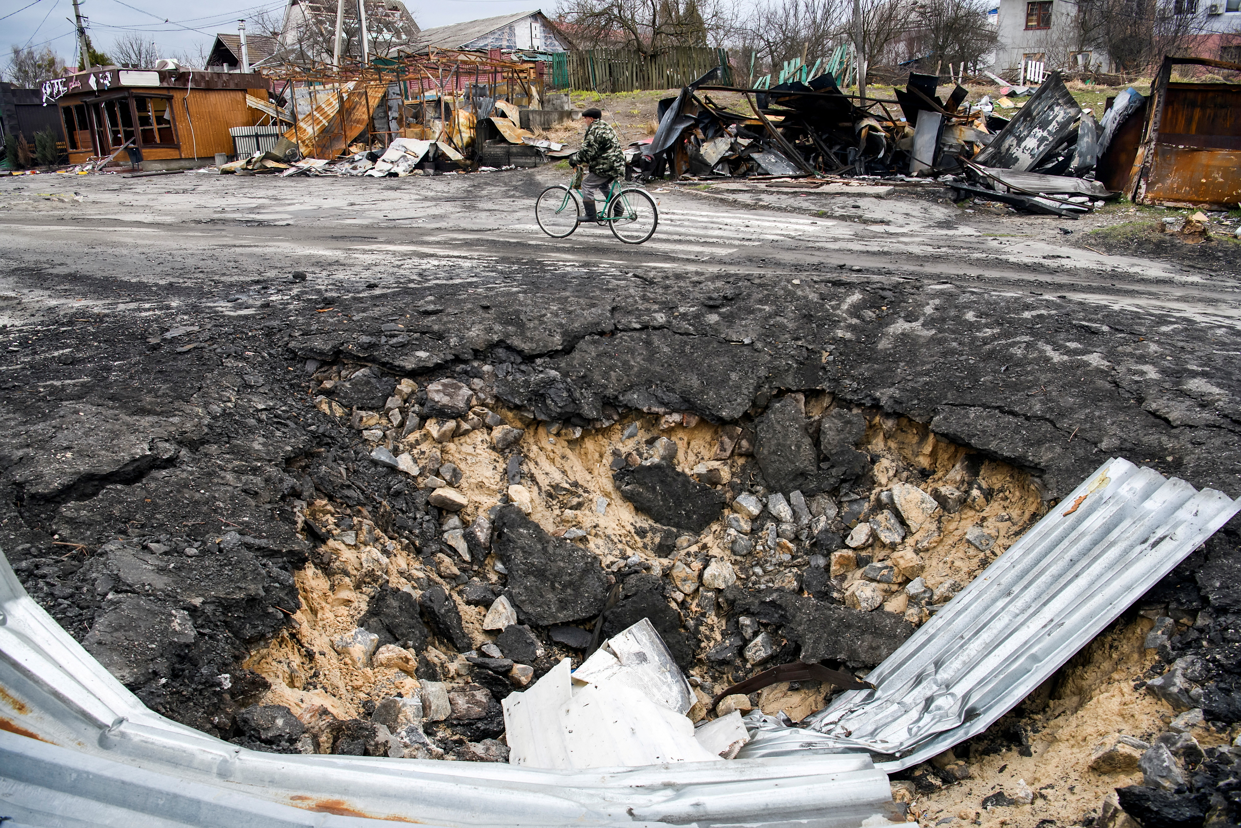 Un ciclista pasa cerca del cráter de una bomba en Demydiv, en las afueras de Kiev (REUTERS/Vladyslav Musiienko)